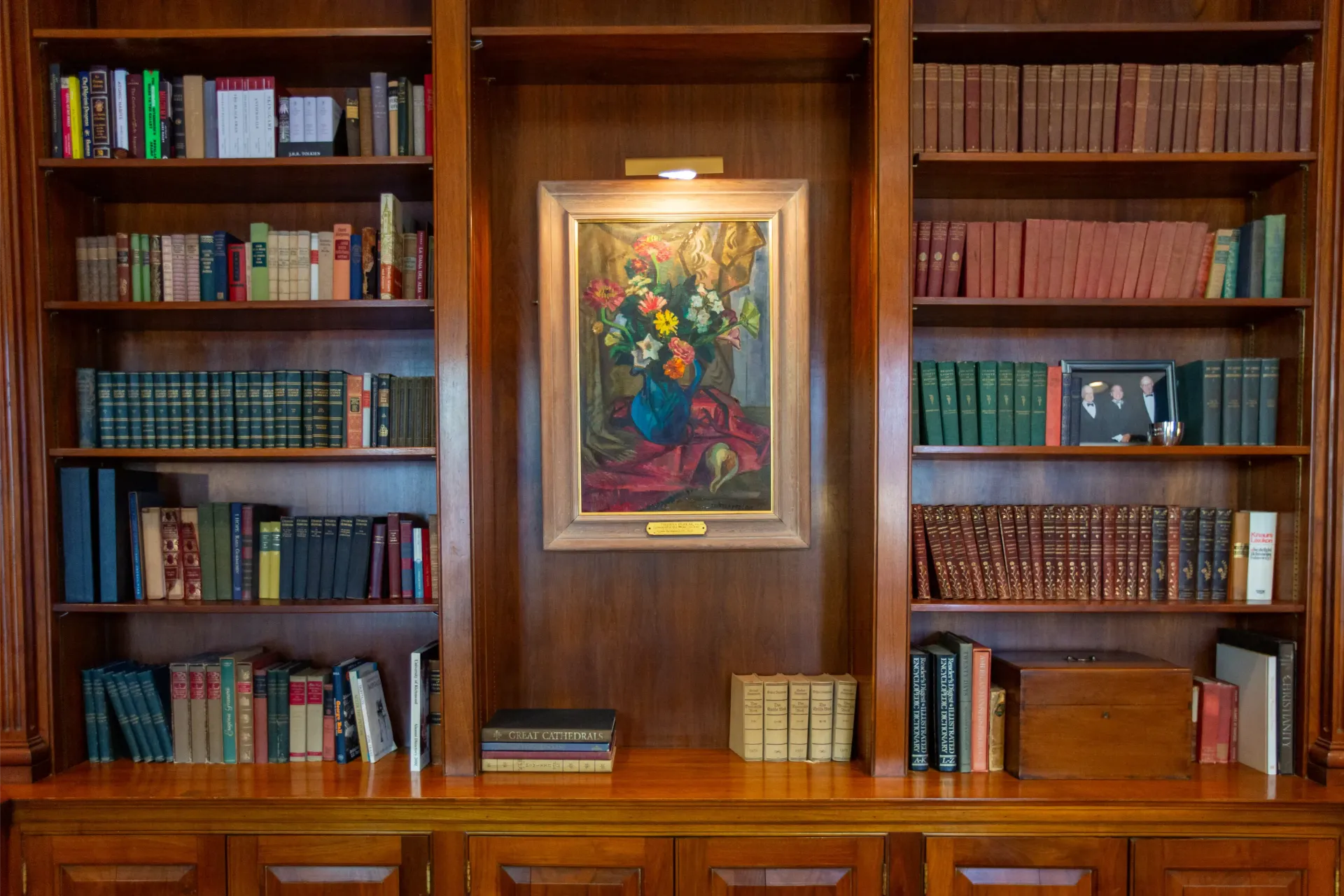 Wooden bookshelf with framed artwork centered, filled with books.