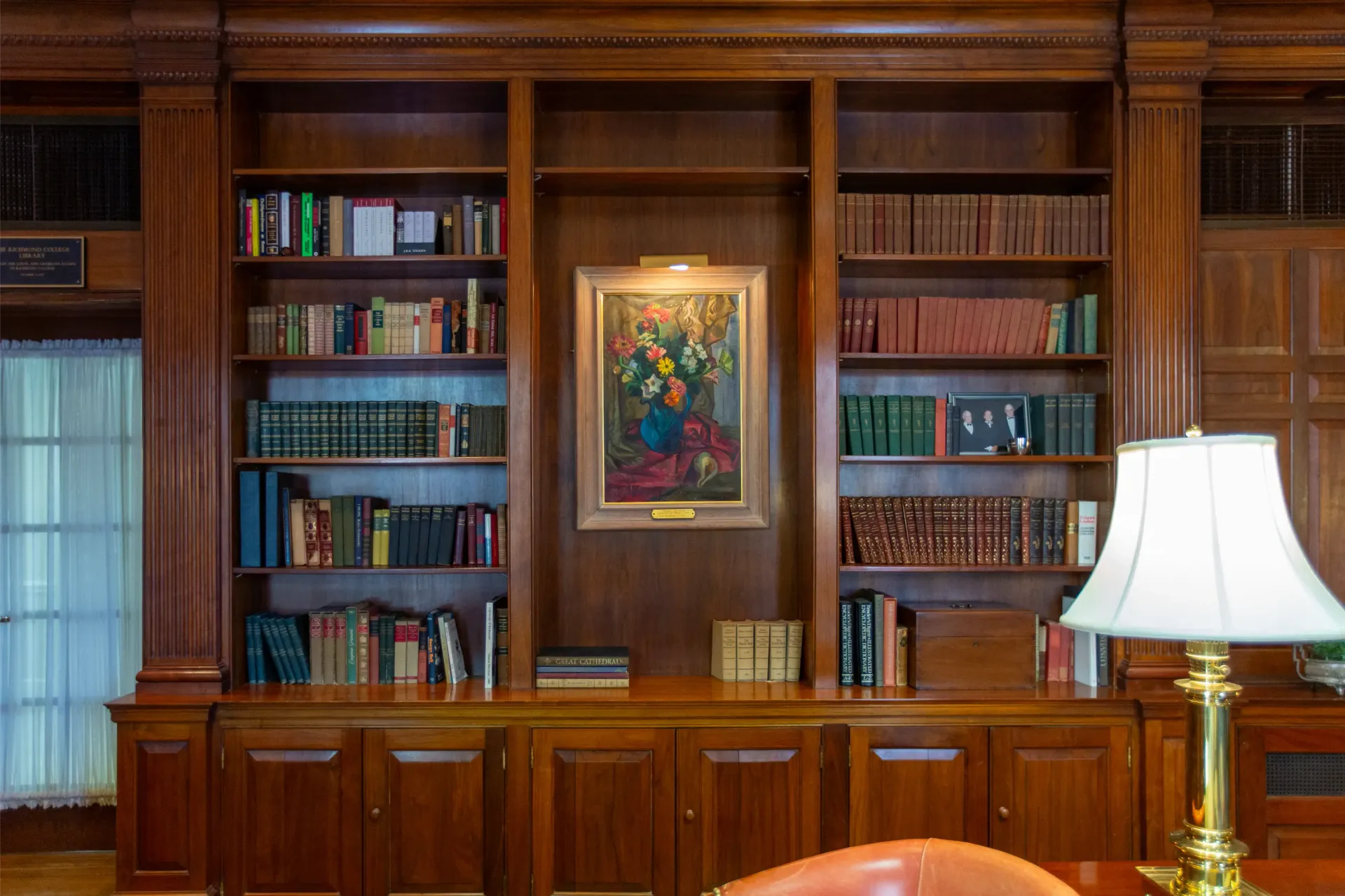 Wooden bookshelves with books, a painting, and a lamp.