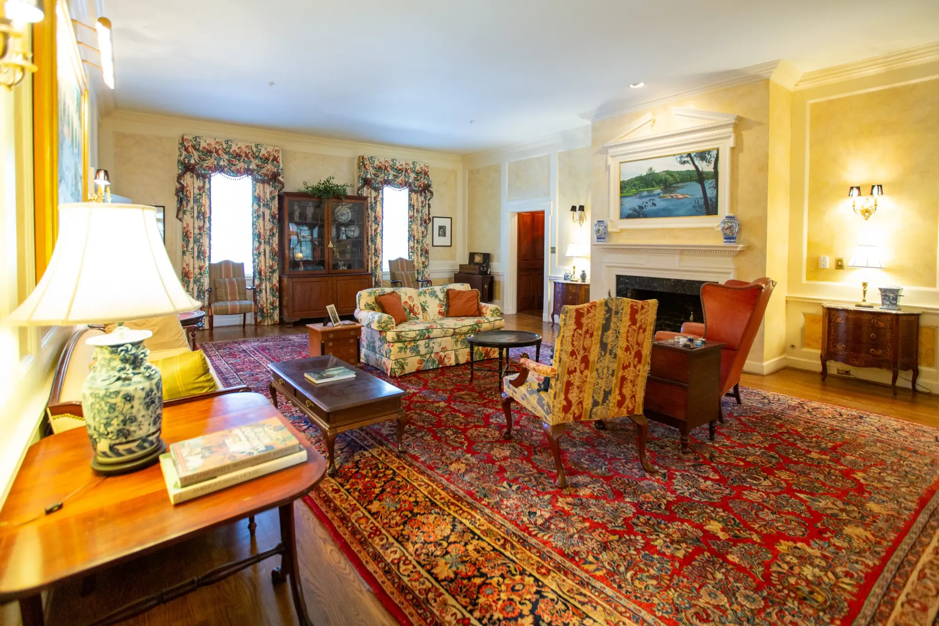 Living room with floral sofas, patterned chairs, fireplace, and large red rug.