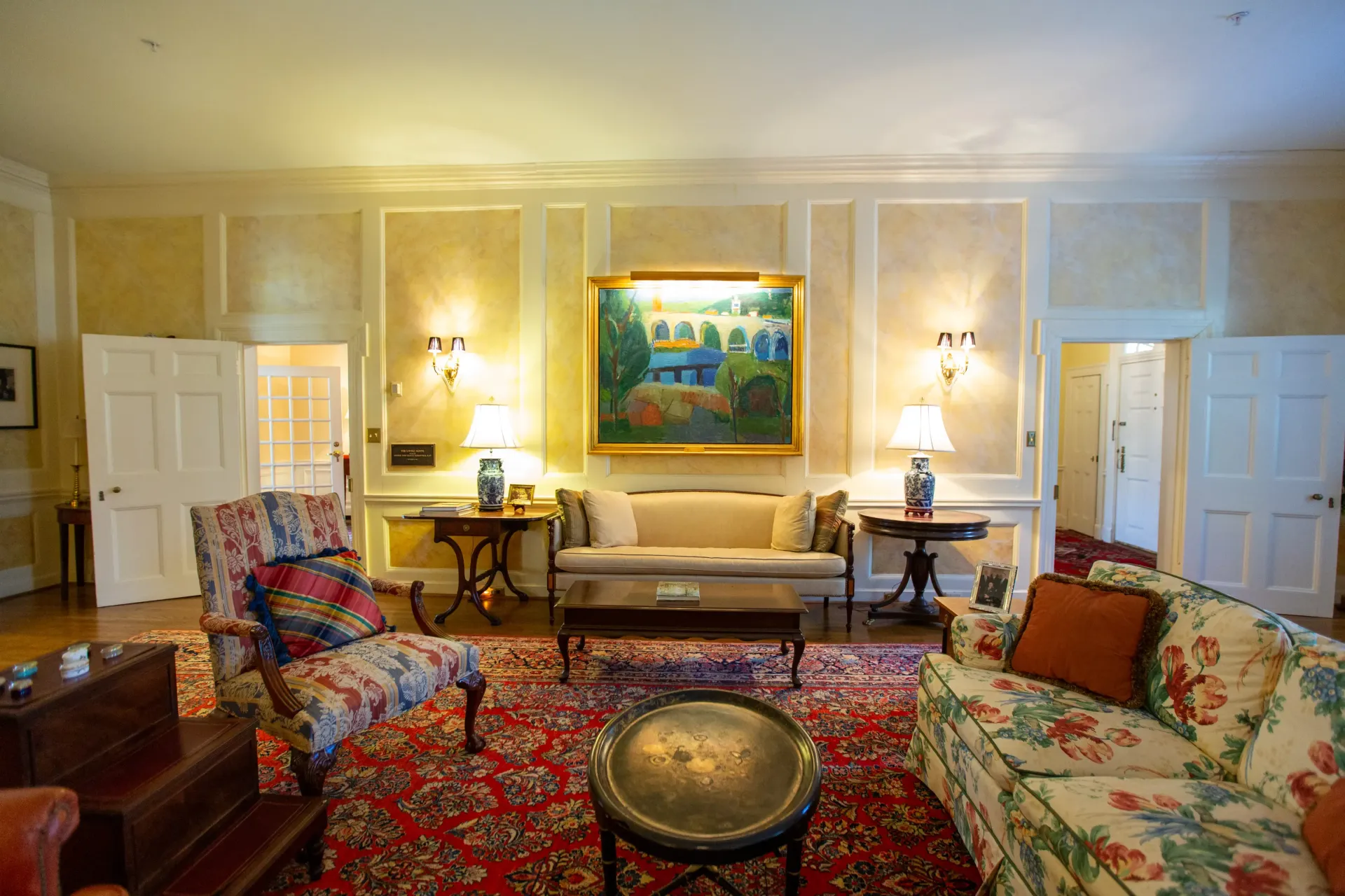 Elegant living room with floral patterned furniture, oriental rug, and artwork. Warm lighting.