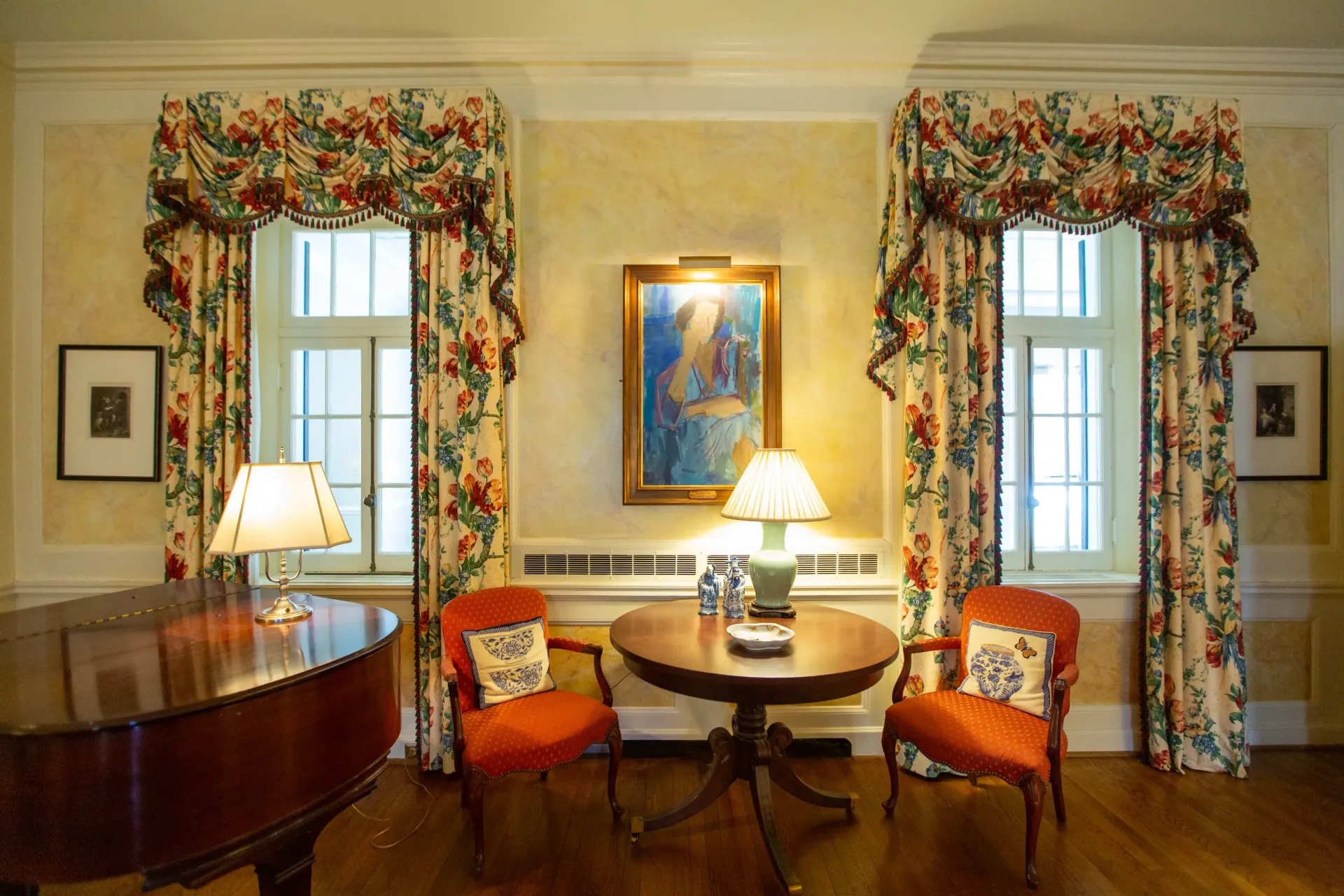 Living room with floral curtains, two red chairs, a round table, and a piano.