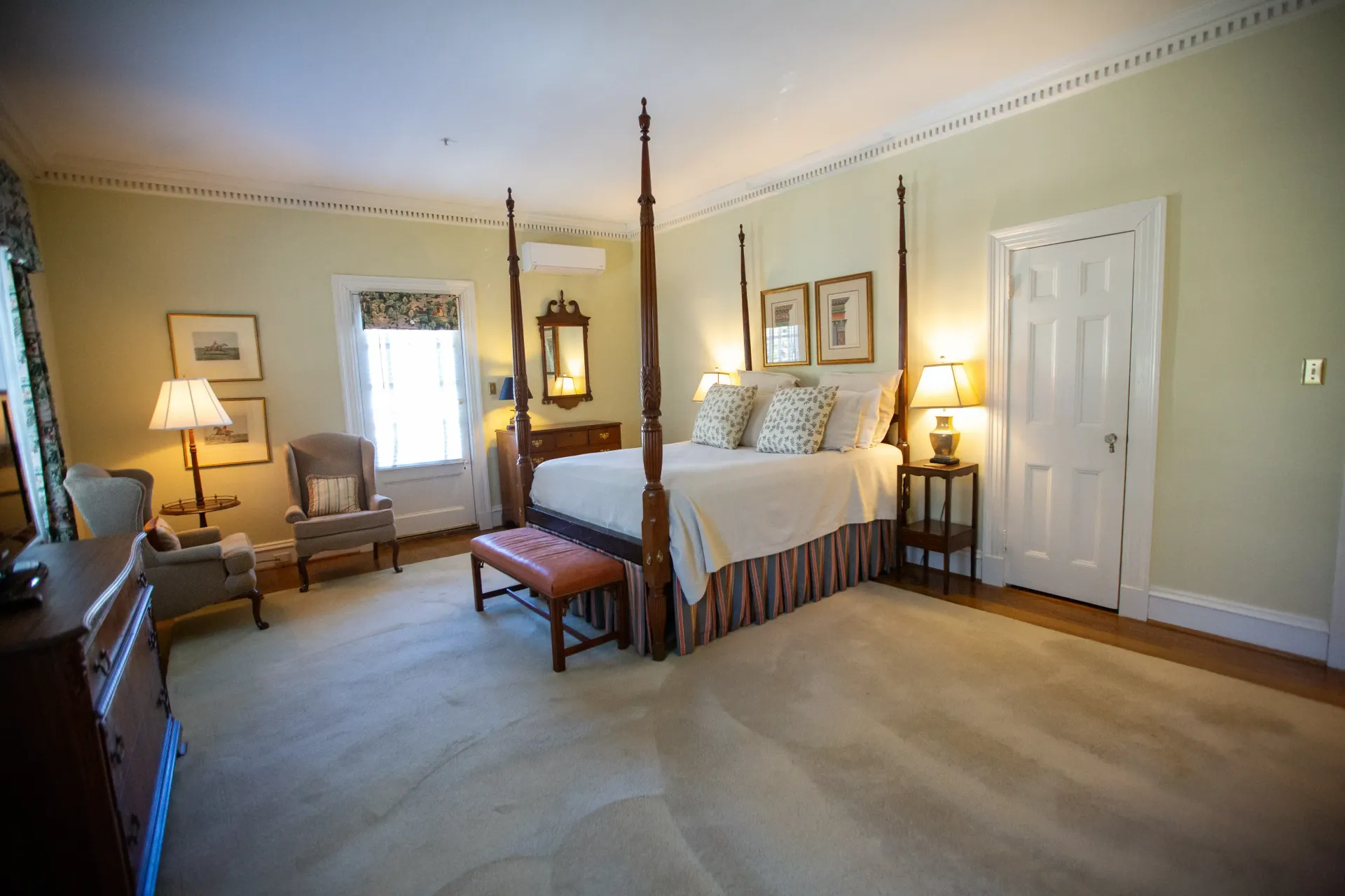 Bedroom with four-poster bed, window, seating area, and traditional decor in light colors.