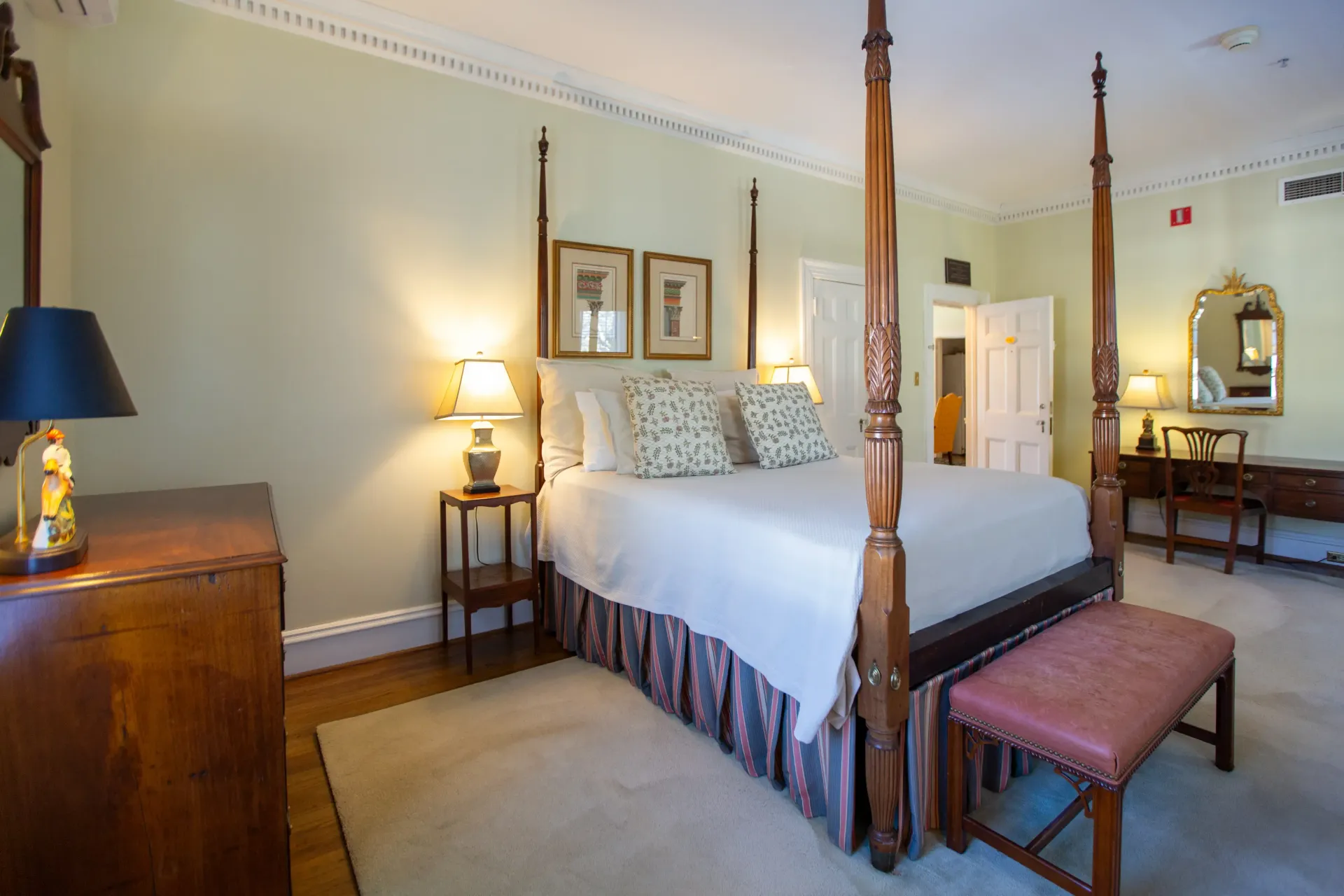Bedroom with four-poster bed, rug, dresser, vanity, and lamps; light green walls, cream molding.