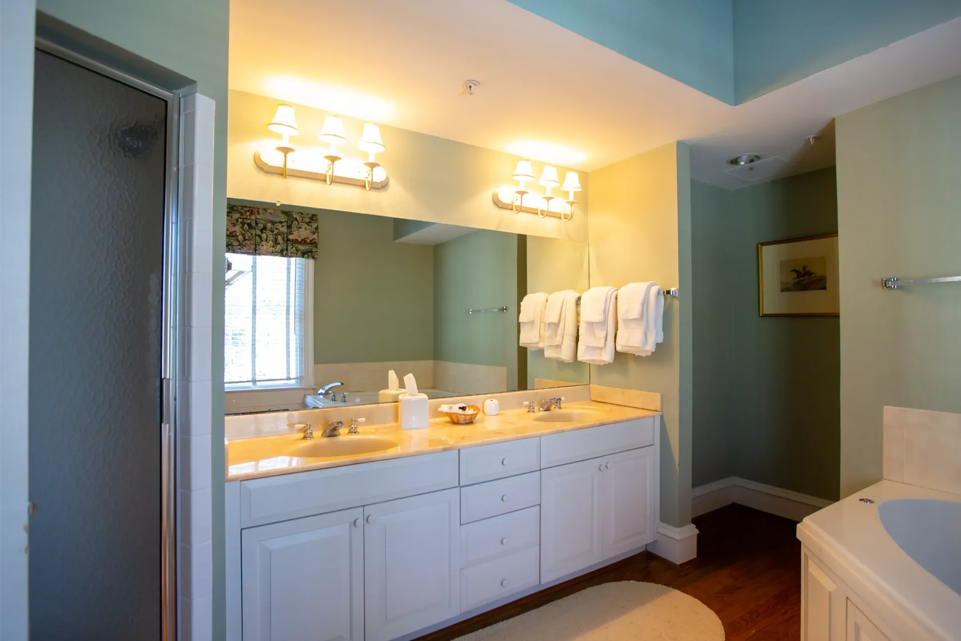Bathroom with white vanity, double sinks, and a shower; light green walls, a window, and a bathtub.