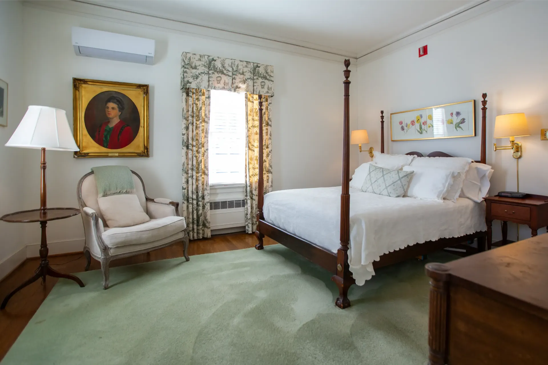 Bedroom with four-poster bed, armchair, art, green rug, and curtains.
