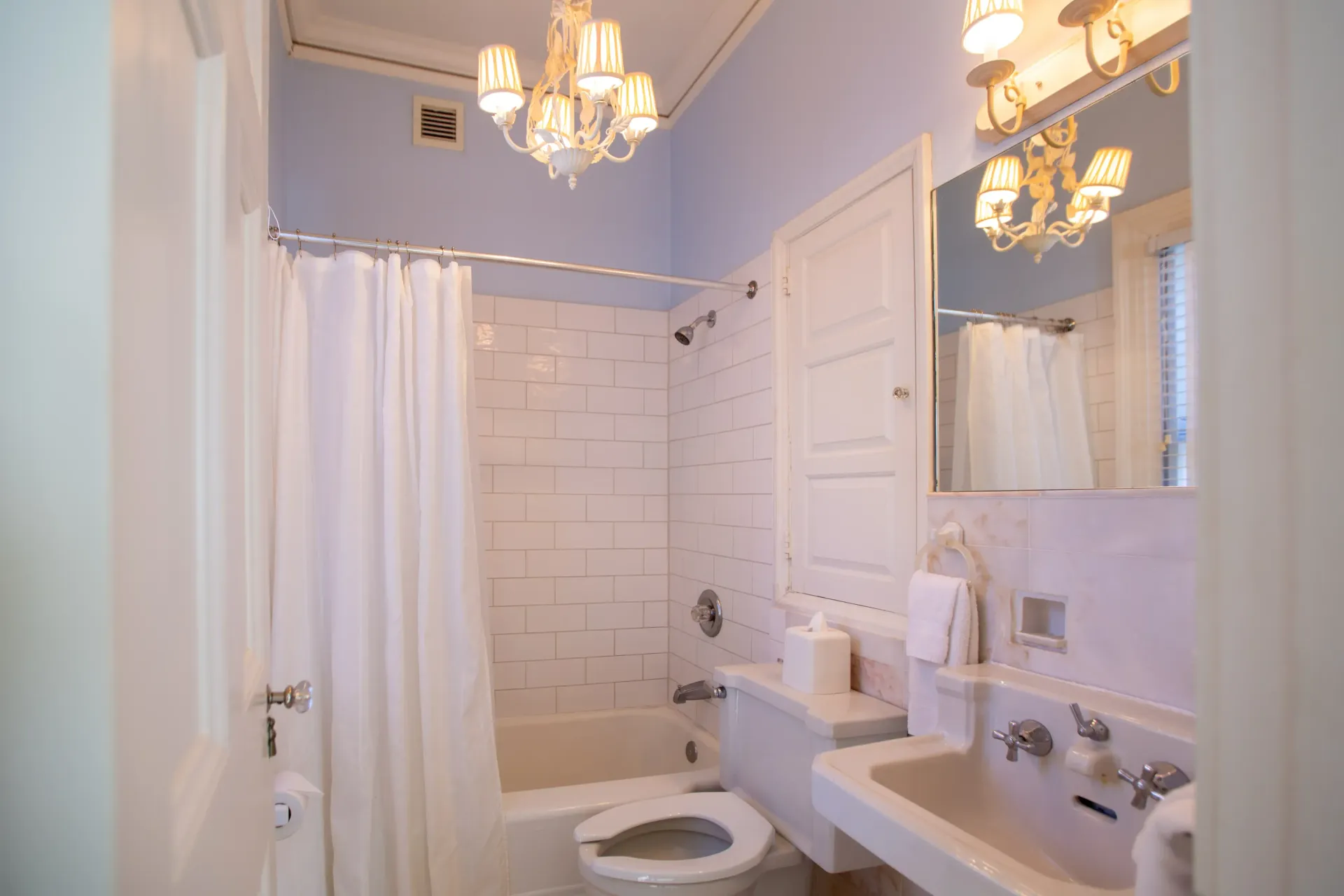 Small bathroom with white fixtures, shower curtain, and a chandelier.