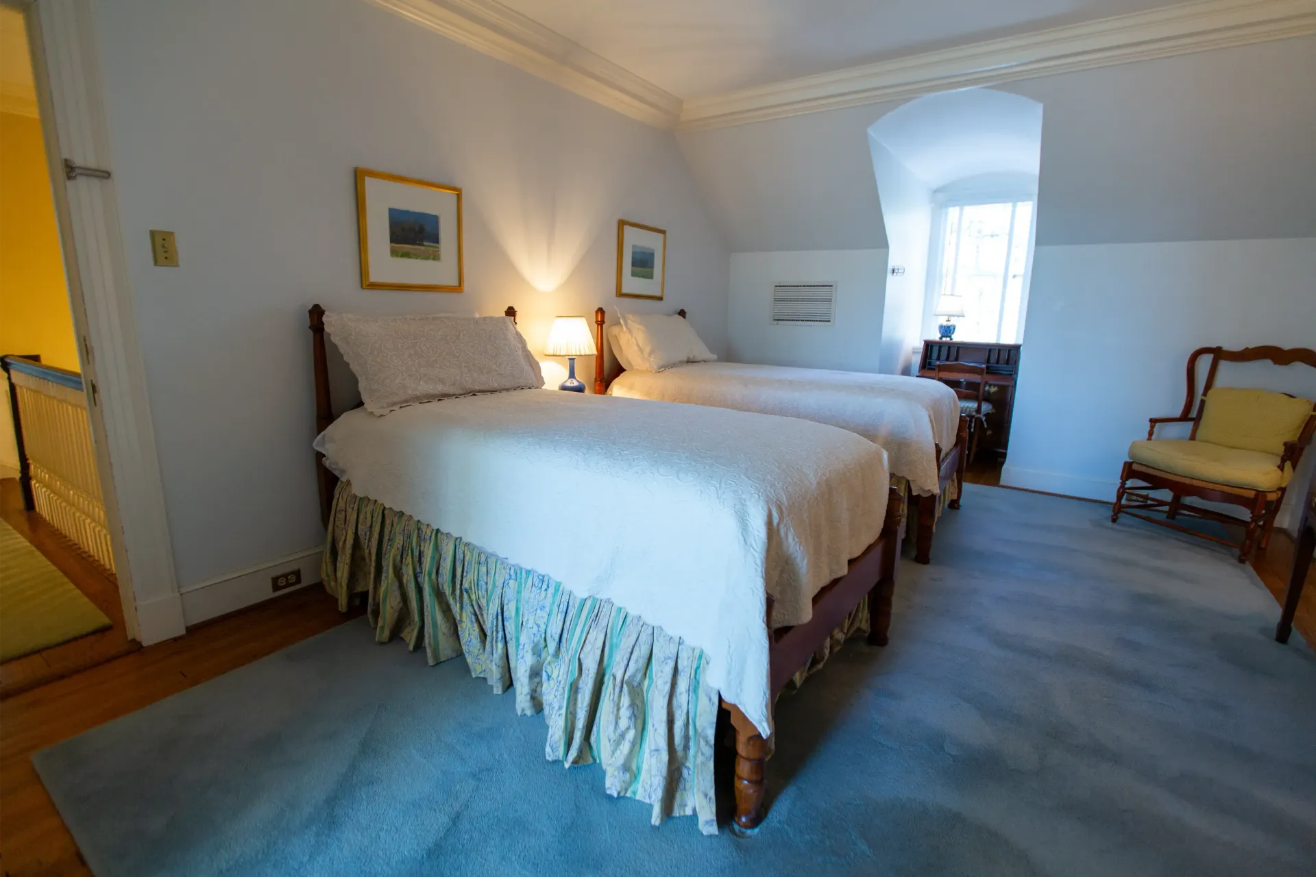 Bedroom with two twin beds, blue rug, small chair, and artwork on the walls.