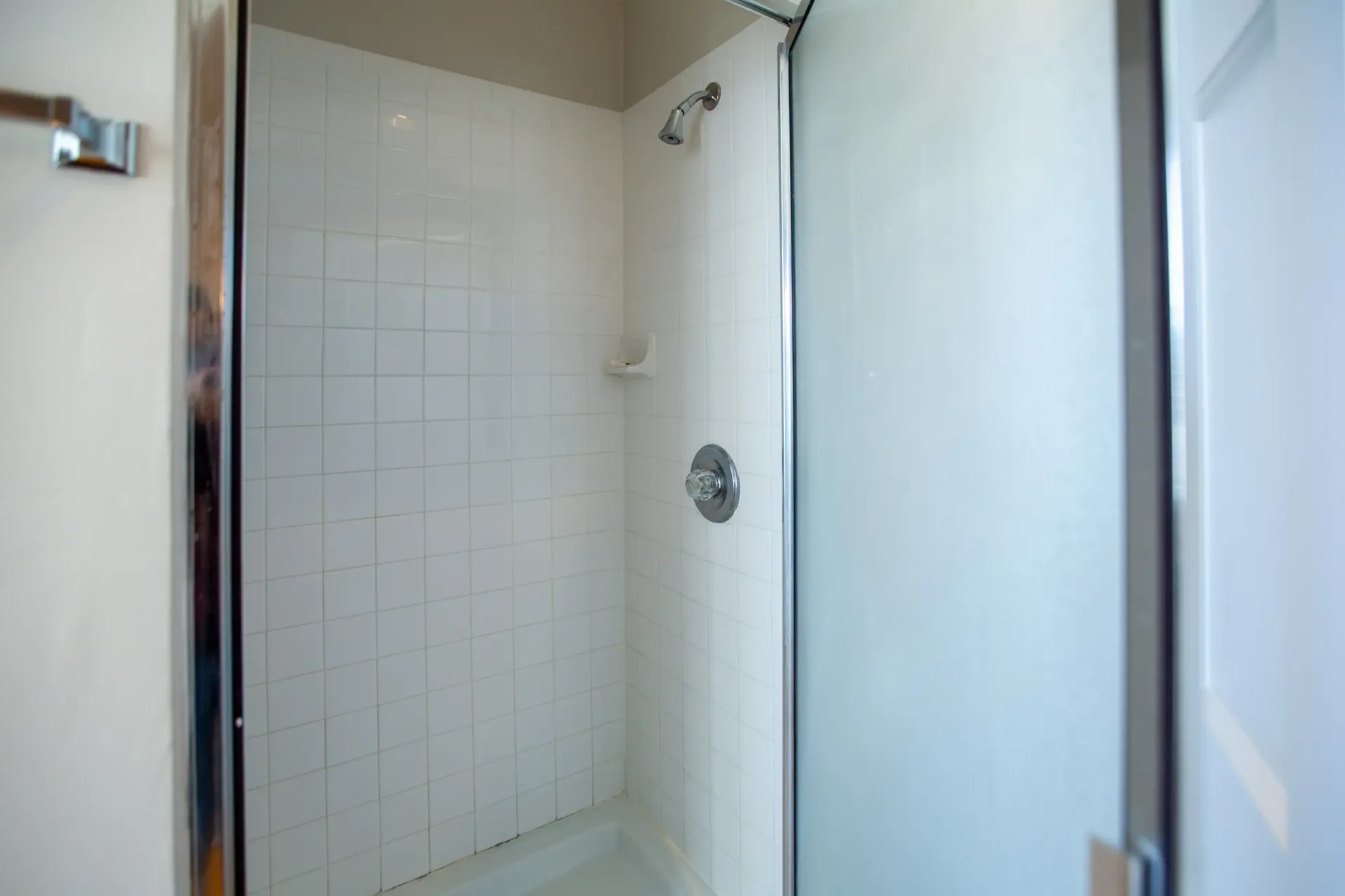 White-tiled shower with a frosted glass door, silver fixtures, and a soap dish.