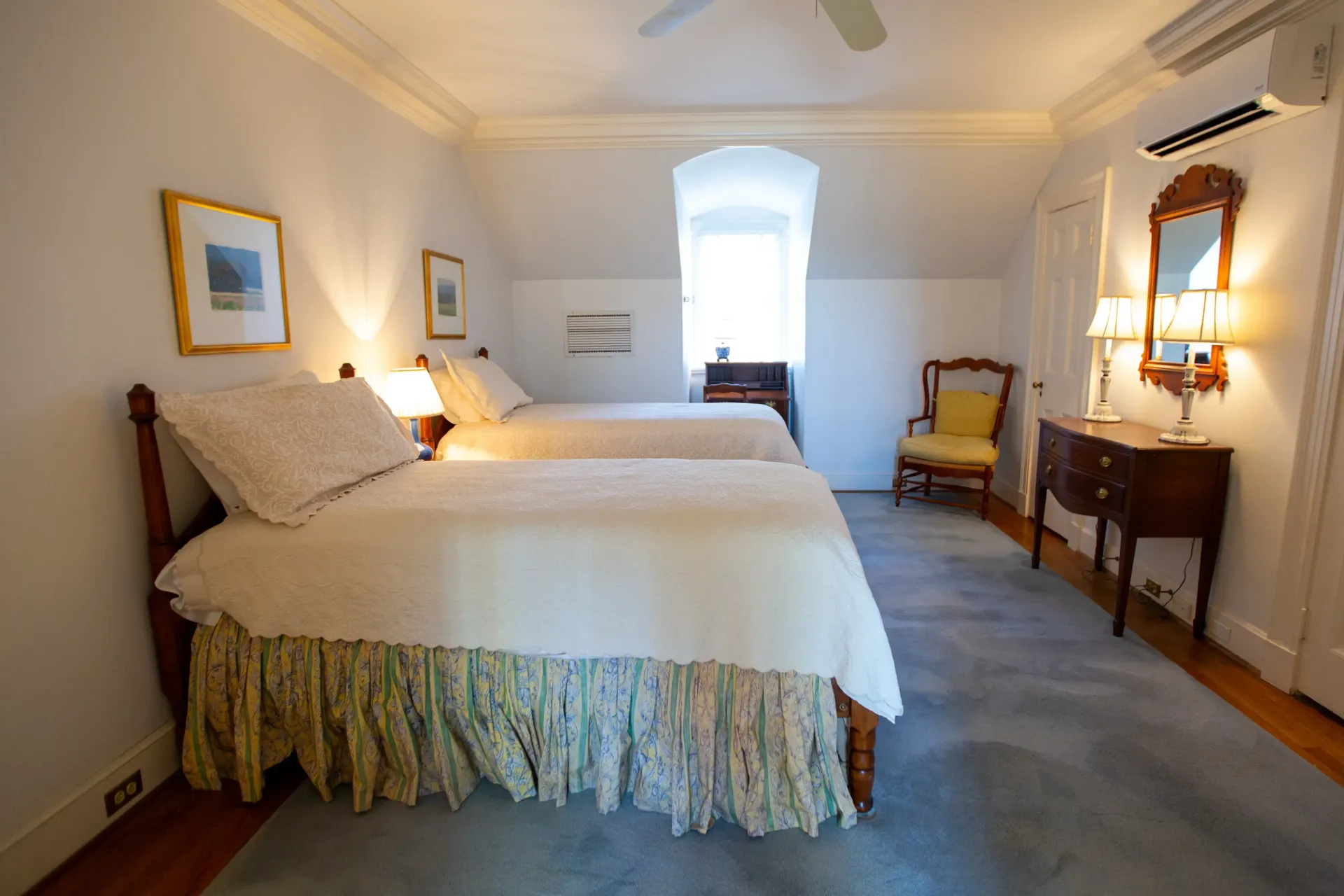 Bedroom with two twin beds, small desk, chair, and a decorative mirror, with soft lighting and a muted blue rug.