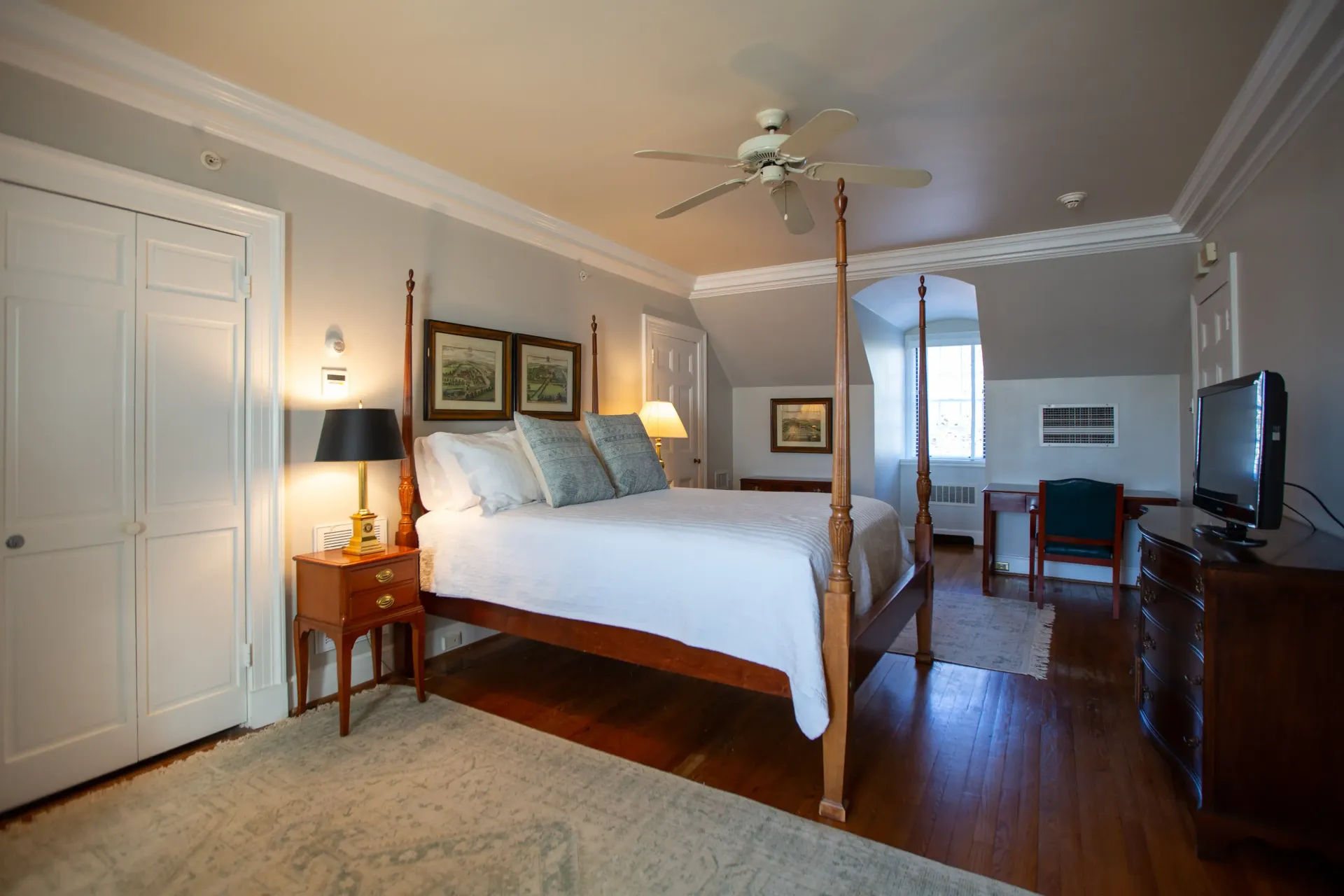 Bedroom with a four-poster bed, wood floors, and neutral walls. A TV sits on a dresser.