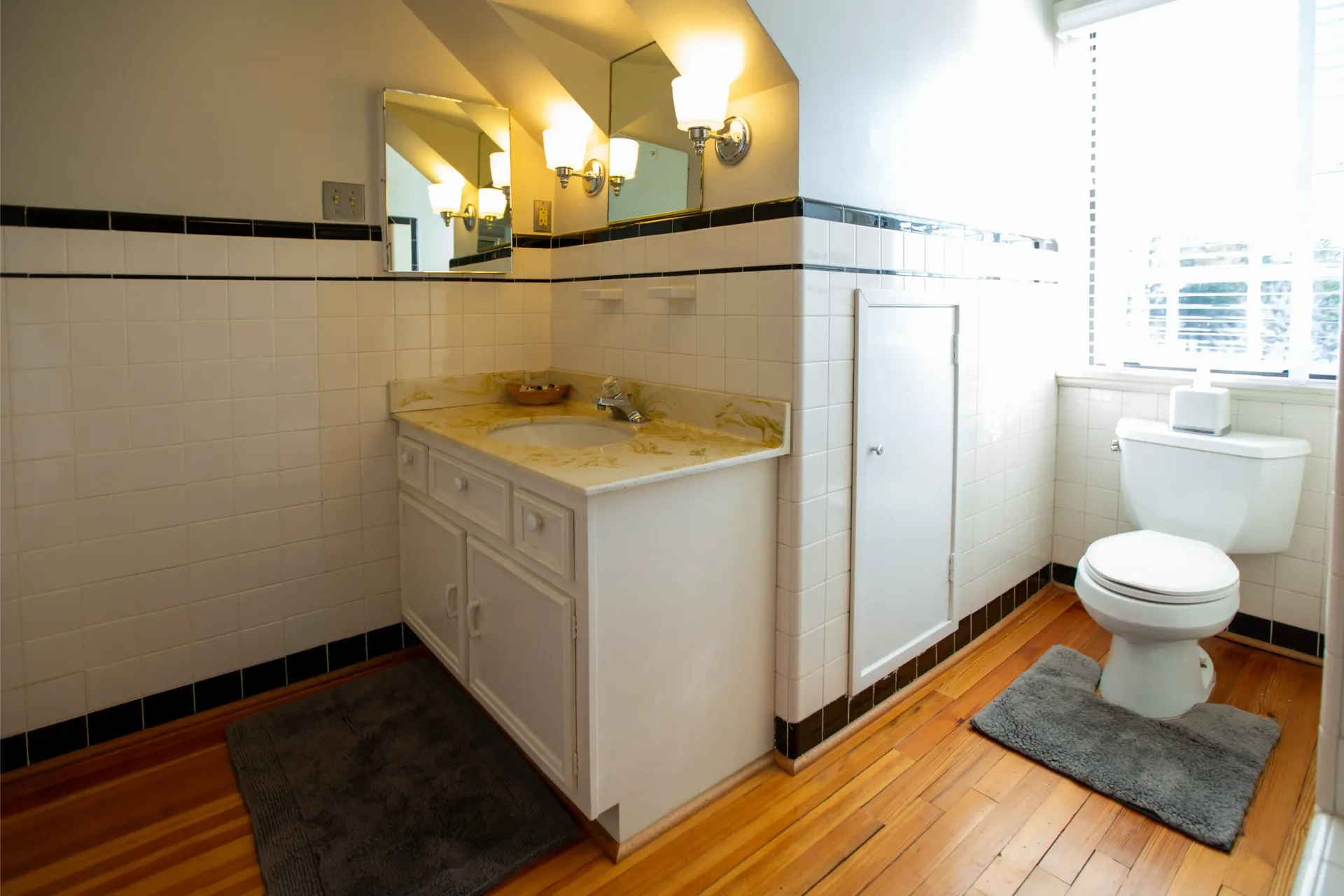 Bathroom with white tile, vanity, toilet, and window. Black trim and gray rug.