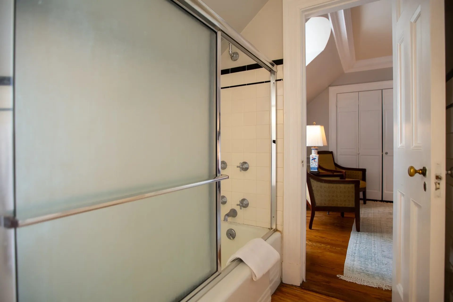 Bathroom with a frosted glass shower door open to a bedroom with wood floors and a closet.
