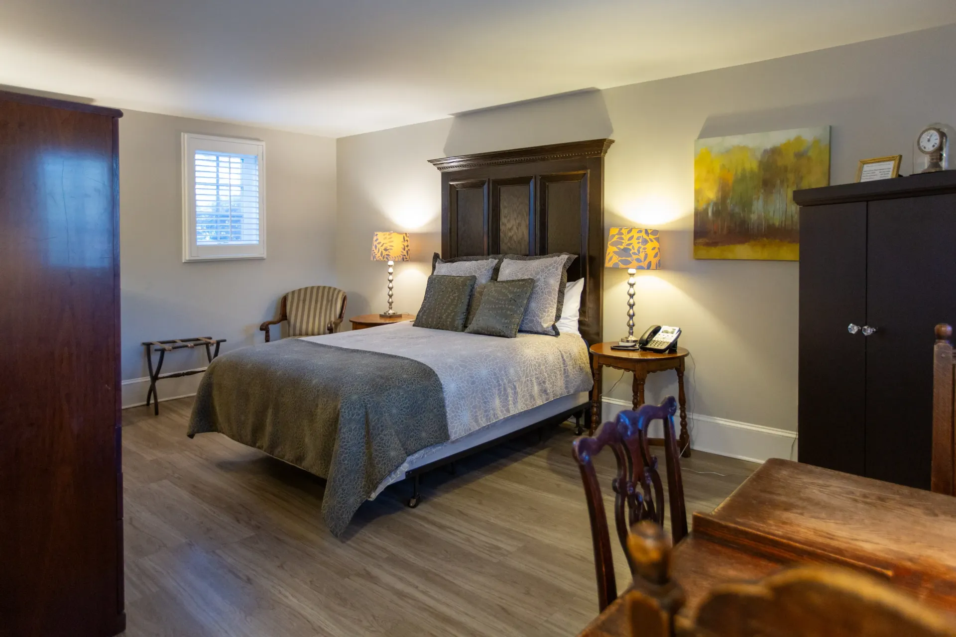 Bedroom with bed, desk, armoire, lamps, and small window.
