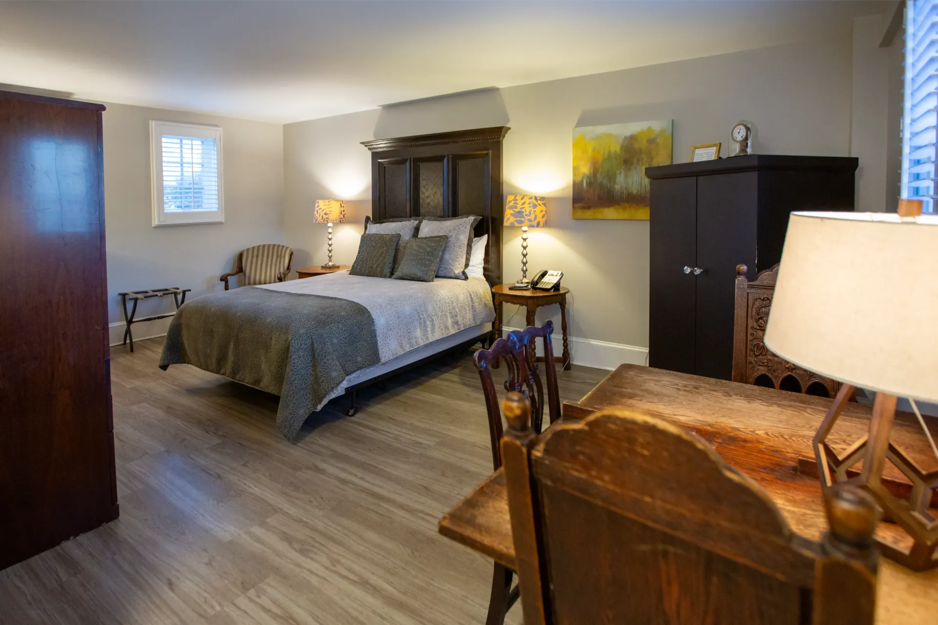 Hotel room with bed, desk, armoire, and two lamps. Soft lighting, neutral colors.