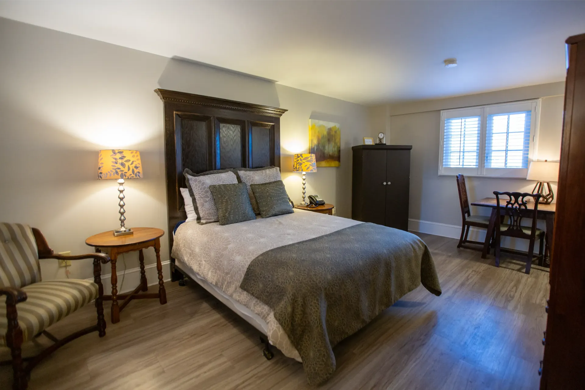 Bedroom with bed, nightstands, chair, desk, and wardrobe. Natural light from a window.