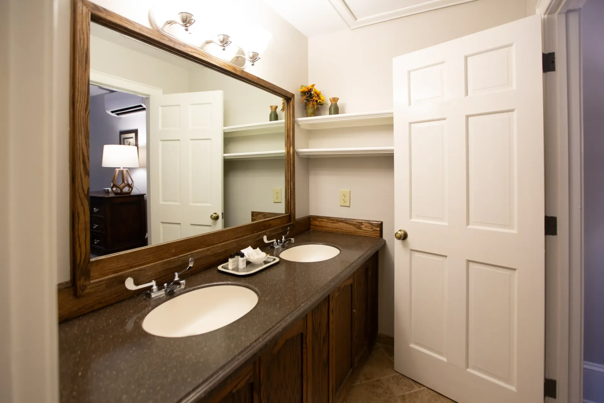 Bathroom with double sinks, large mirror, wooden cabinets, and white door.