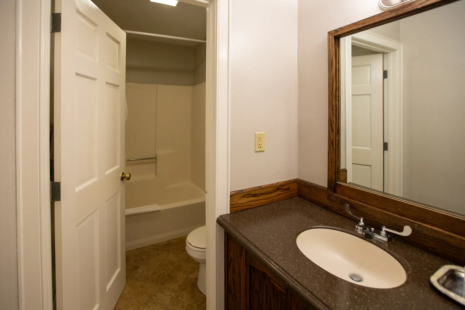 Bathroom with sink, mirror, and a door to a shower/tub area; light-colored walls and floor.