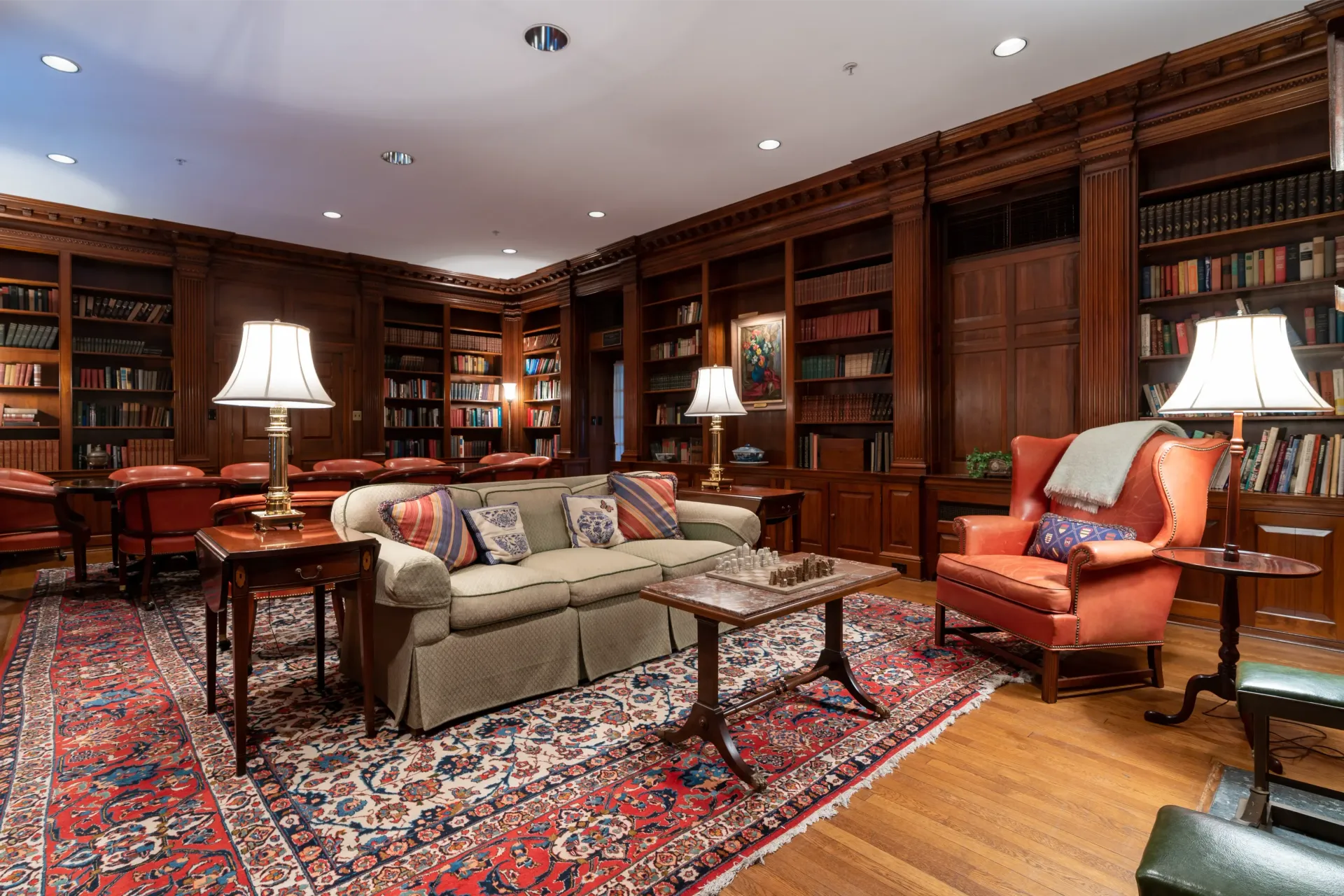 Cozy library with wood paneling, bookshelves, a patterned rug, sofa, and chairs.