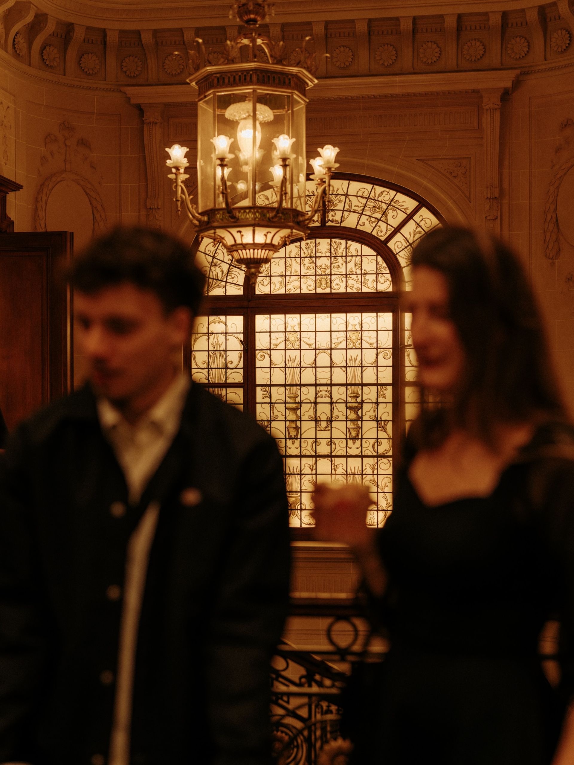 Woman's hand pressing elevator button on gold-colored panel, wearing a light blue suit.