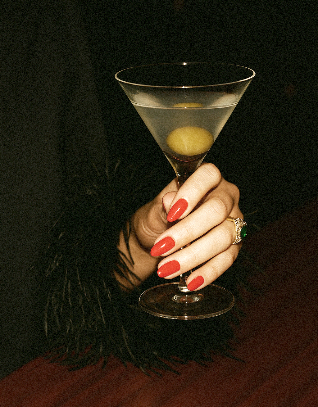 Hand holding a martini glass with a green olive, red nail polish.