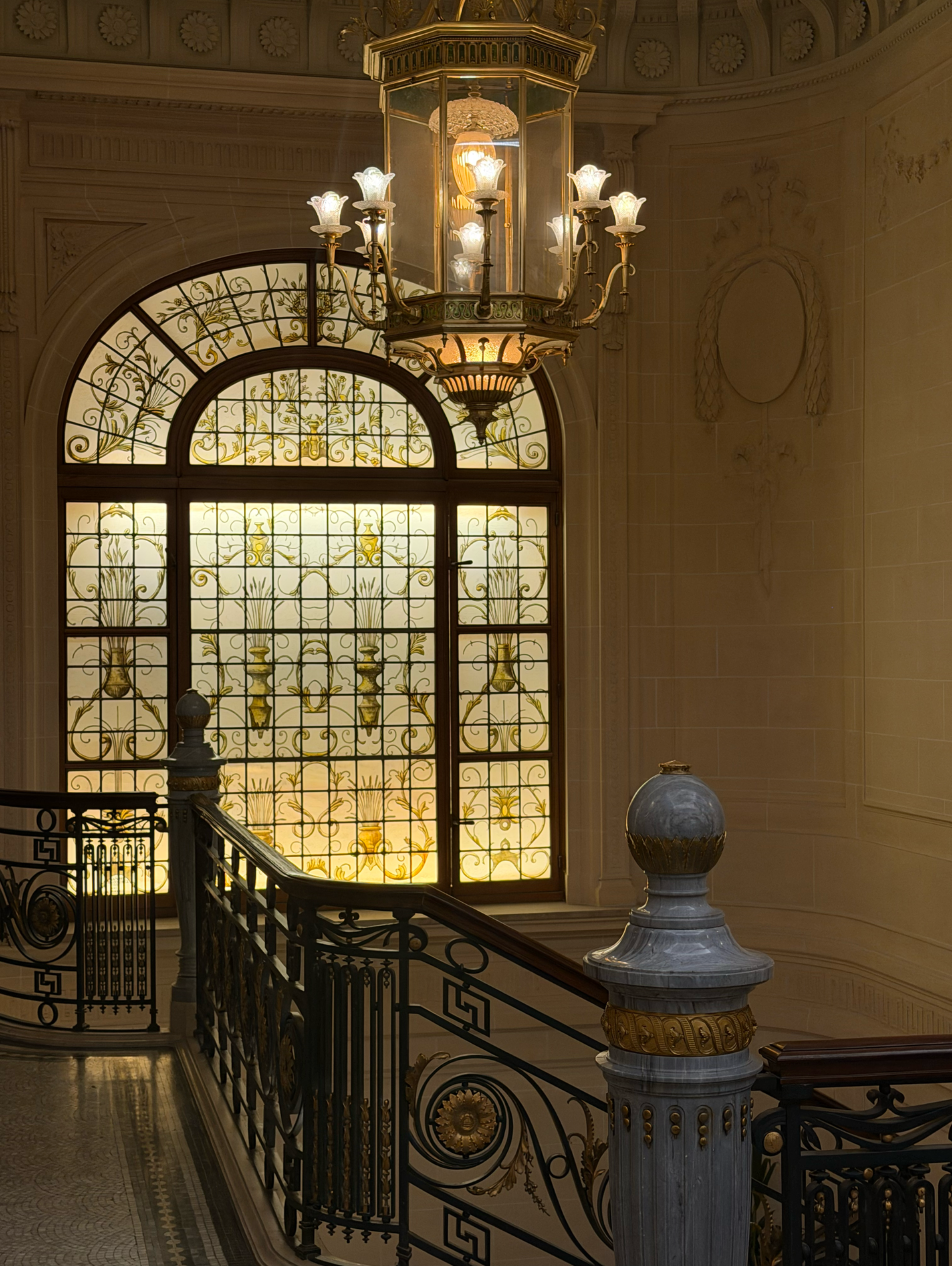 Woman's hand pressing elevator button on gold-colored panel, wearing a light blue suit.