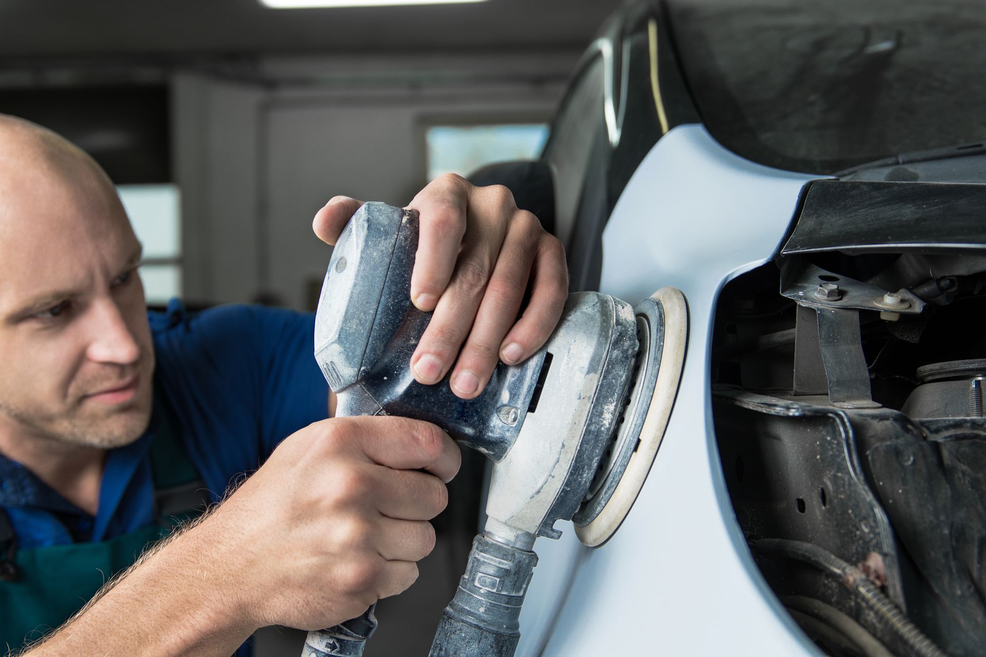 Grinder in the hands of a man who sharpens a car's varnish in the car shop.