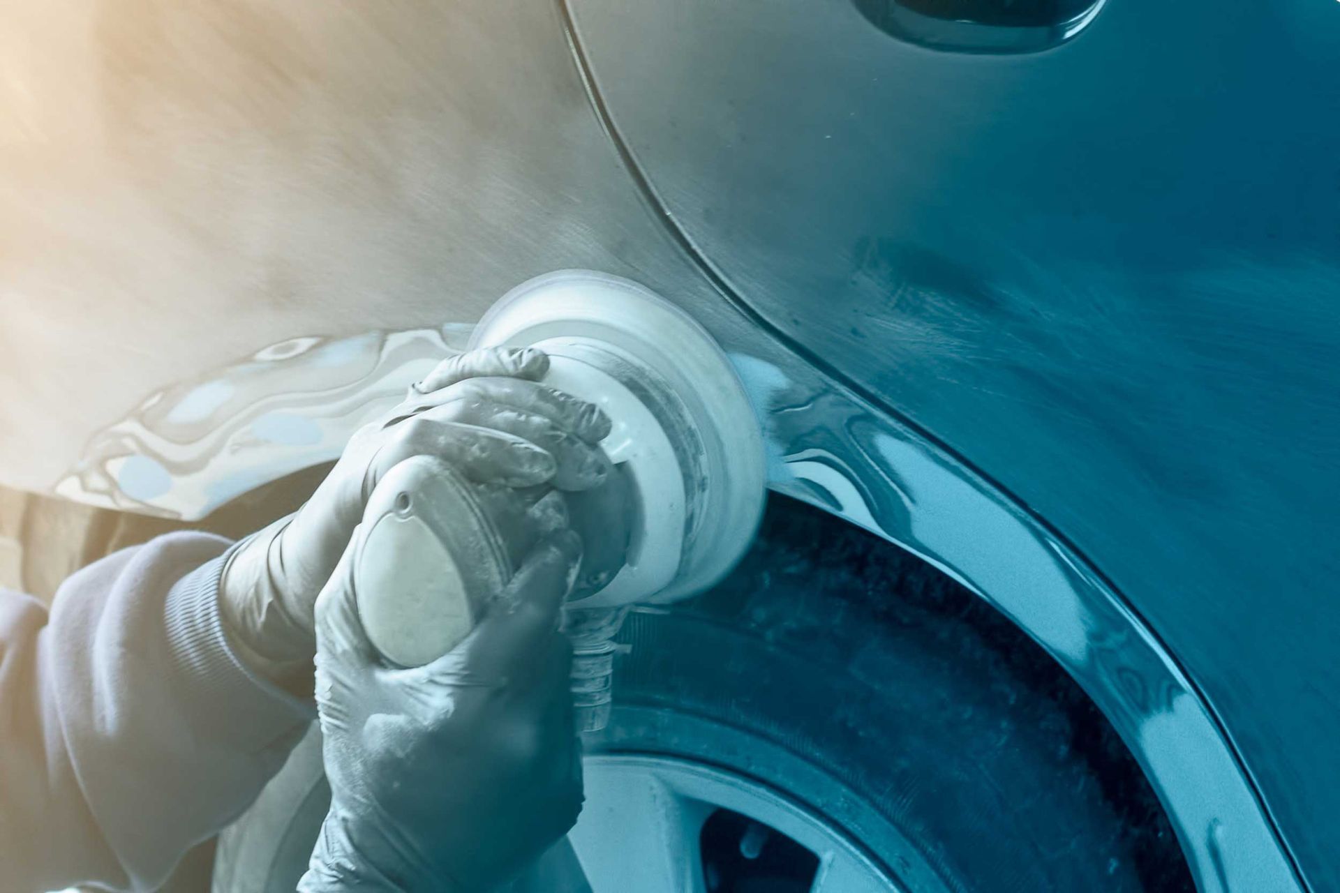 Gloved hands using a rotary polisher on a metallic blue car panel. Gloved hands using a rotary polisher on a metallic blue car panel.