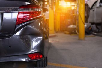 An auto body repair technician fixing collision damage on a vehicle panel in a professional repair shop.