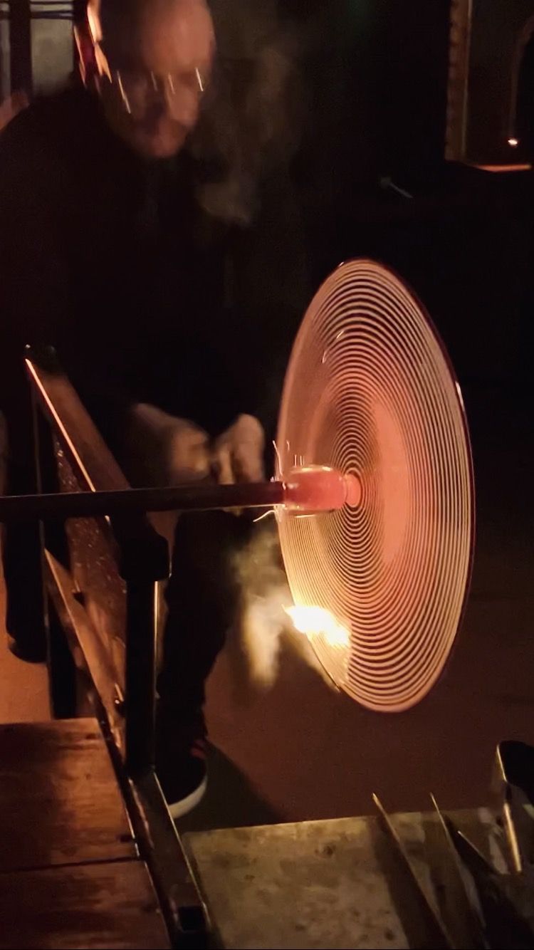A person working with molten glass, shaping a large, radiating circular form.