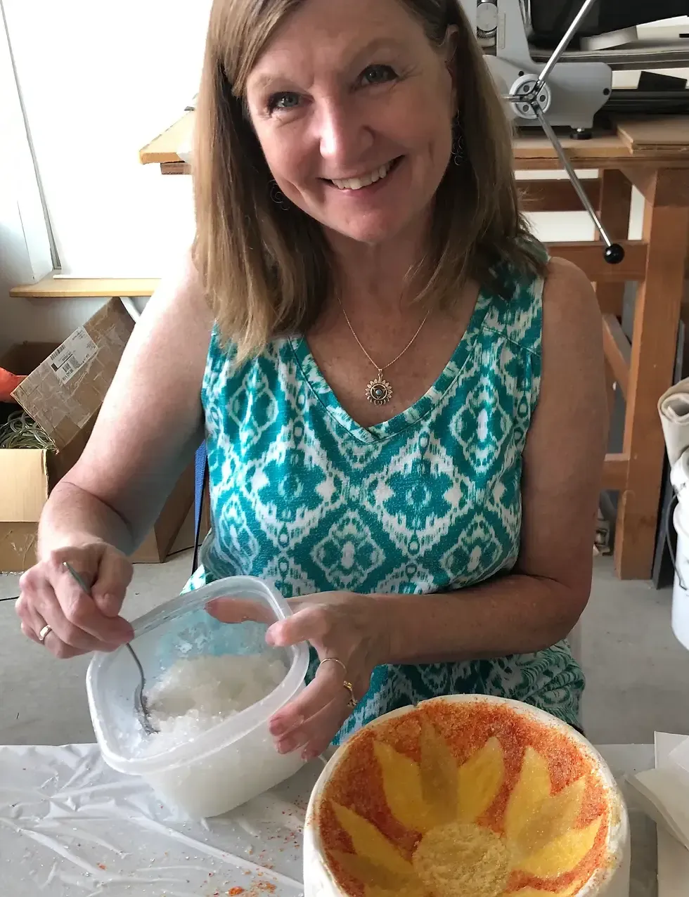 Woman stirring white substance in a container, smiling at the camera, next to a ceramic bowl.