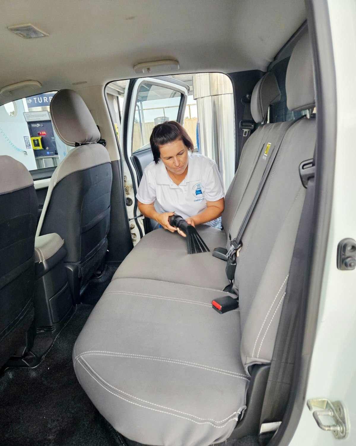 A Woman Is Cleaning The Back Seat Of A White Truck With A Vacuum Cleaner — Carwash 44 In Caboolture, QLD