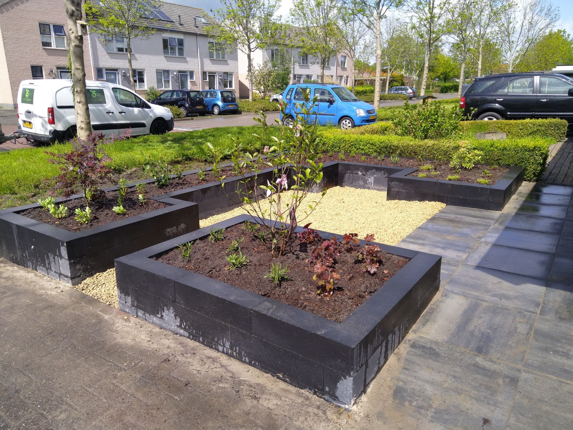Bloembakken met jonge planten en grind langs een stoep in een woonstraat.