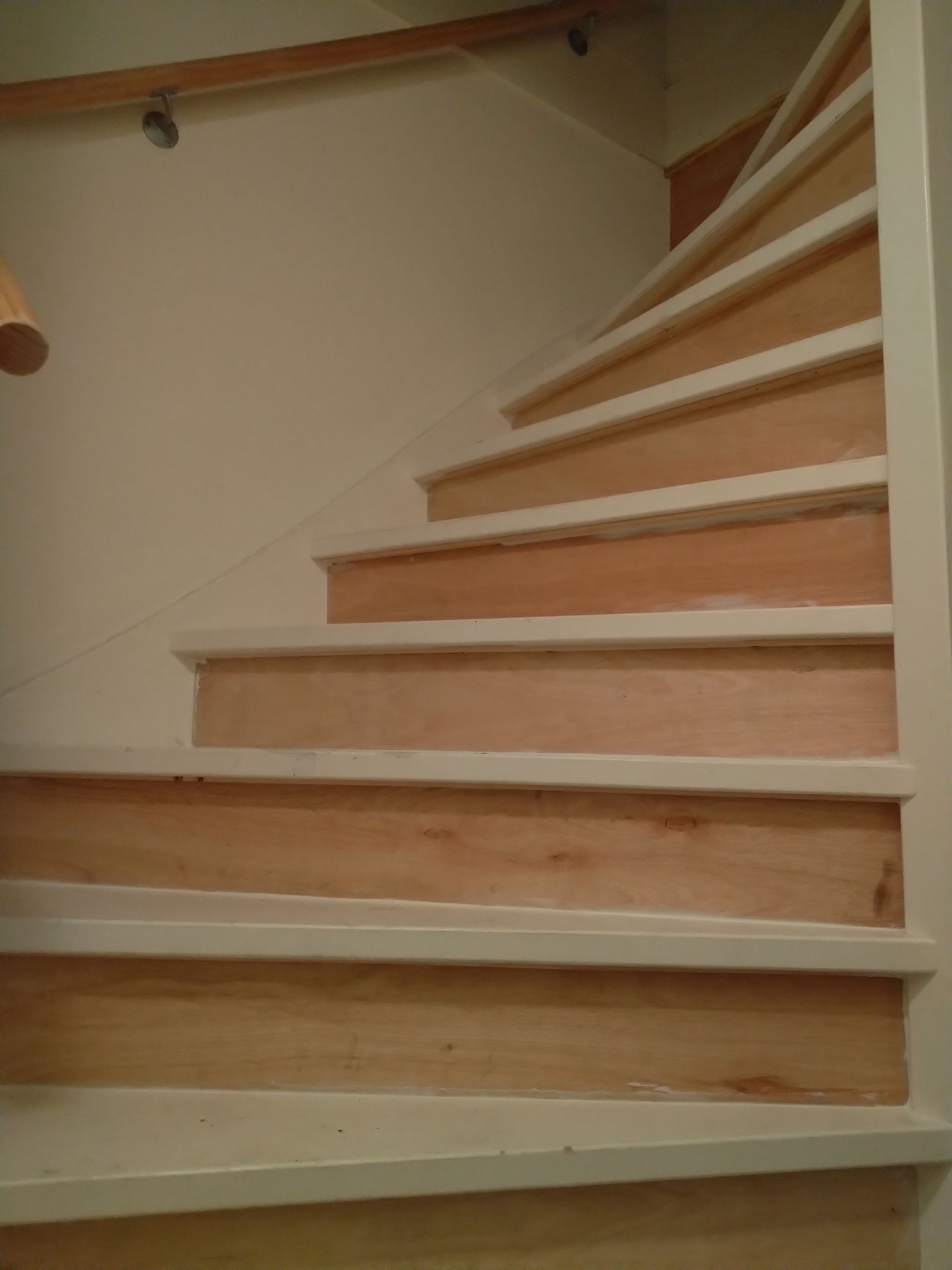 Houten trap met crèmekleurige afwerking en leuning, die omhoog loopt tegen een lichtgekleurde muur.