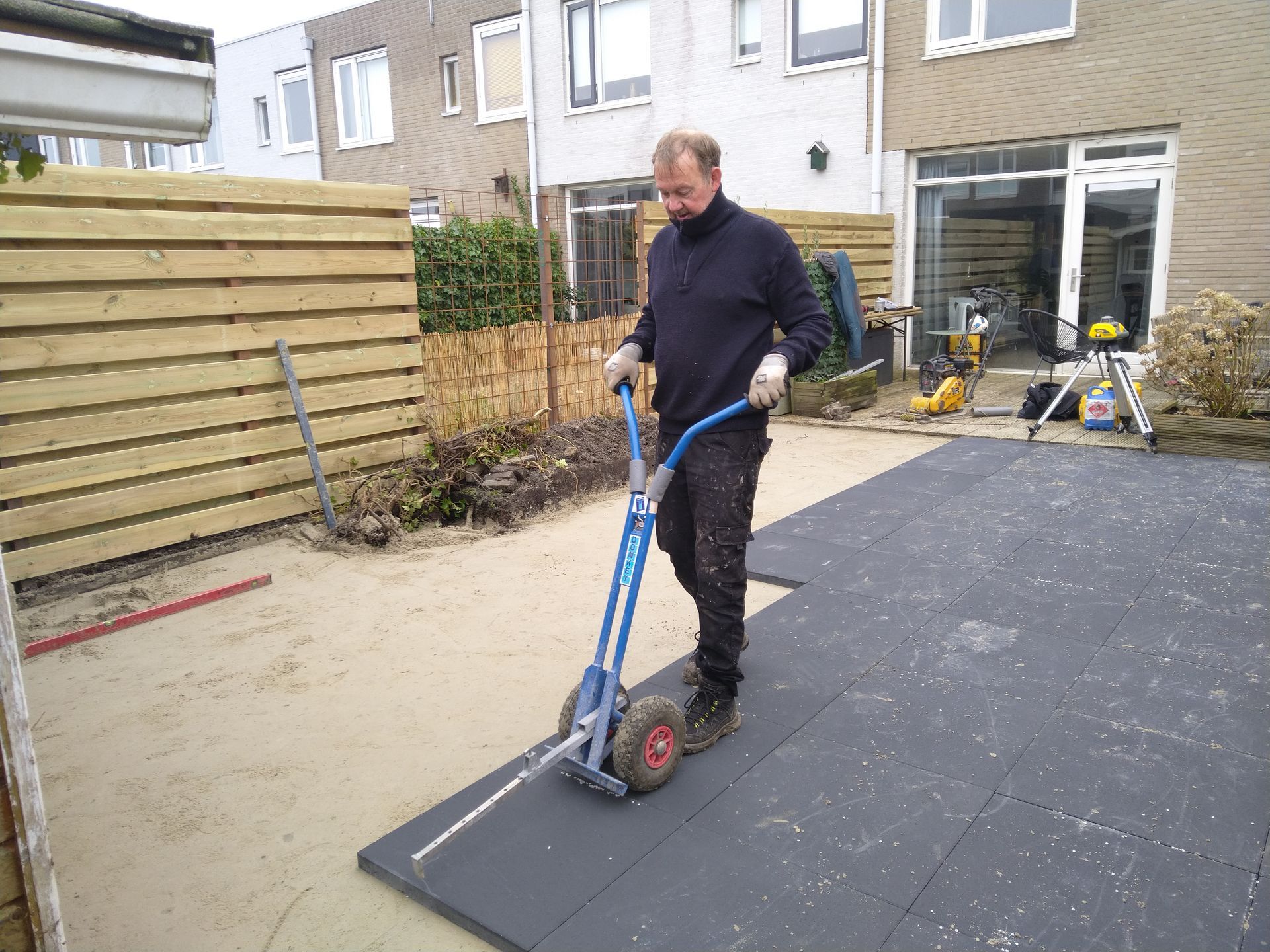 Een man gebruikt een markeerpen op een zwart rubberen oppervlak in een achtertuin.