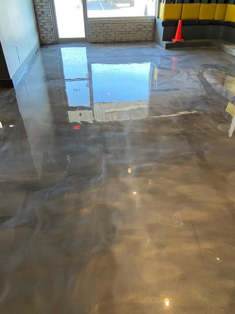 Shiny, metallic epoxy floor reflecting a bright window and the interior of a room, with a brick wall in the background.