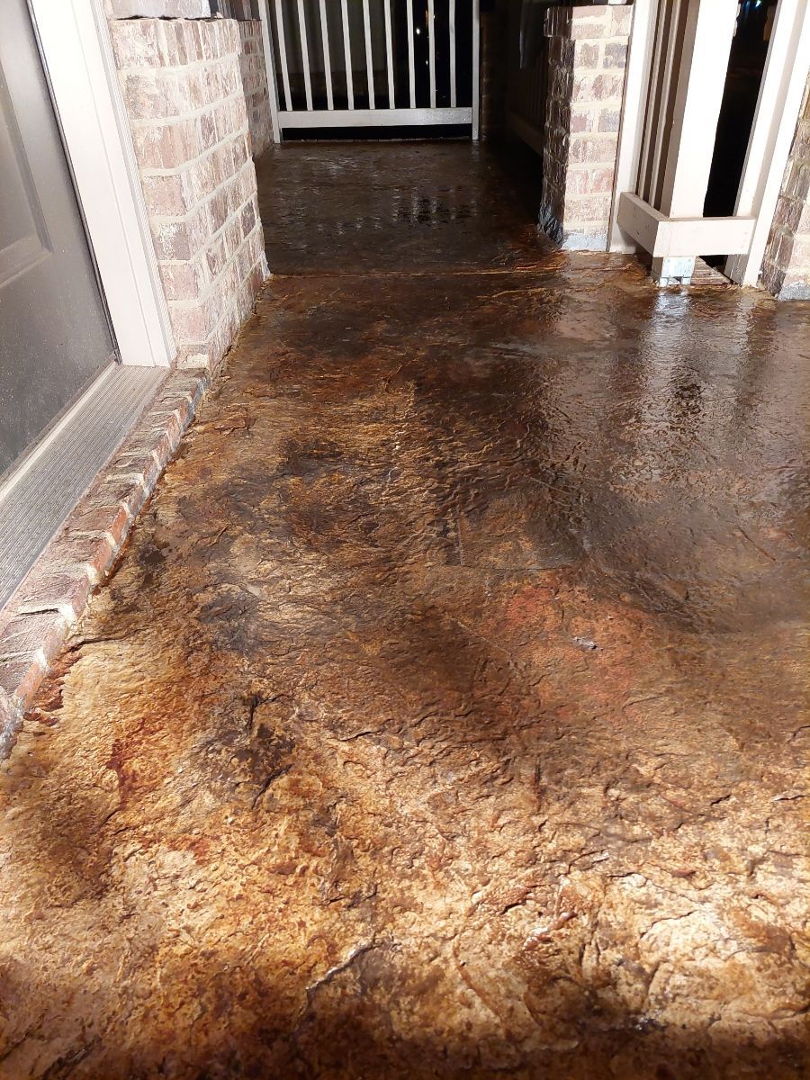 Brown stained concrete patio with brick accents, leading to a doorway and a white fence in the background.