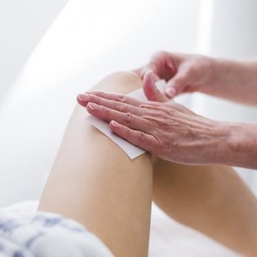 Une personne épile la jambe d'une autre personne avec du papier ciré.