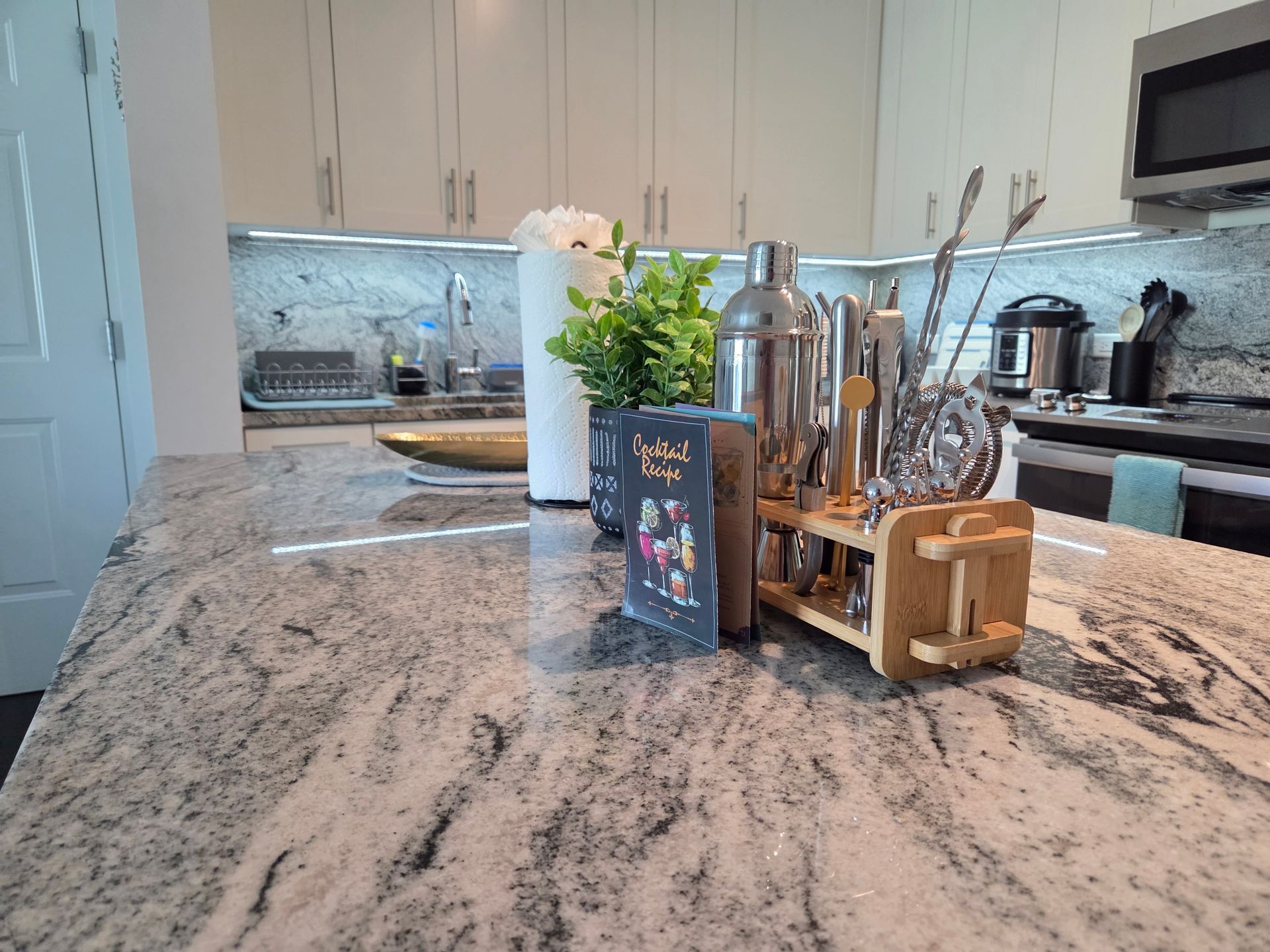 Kitchen counter with bar tools and appliances. White cabinets and a granite countertop are visible.