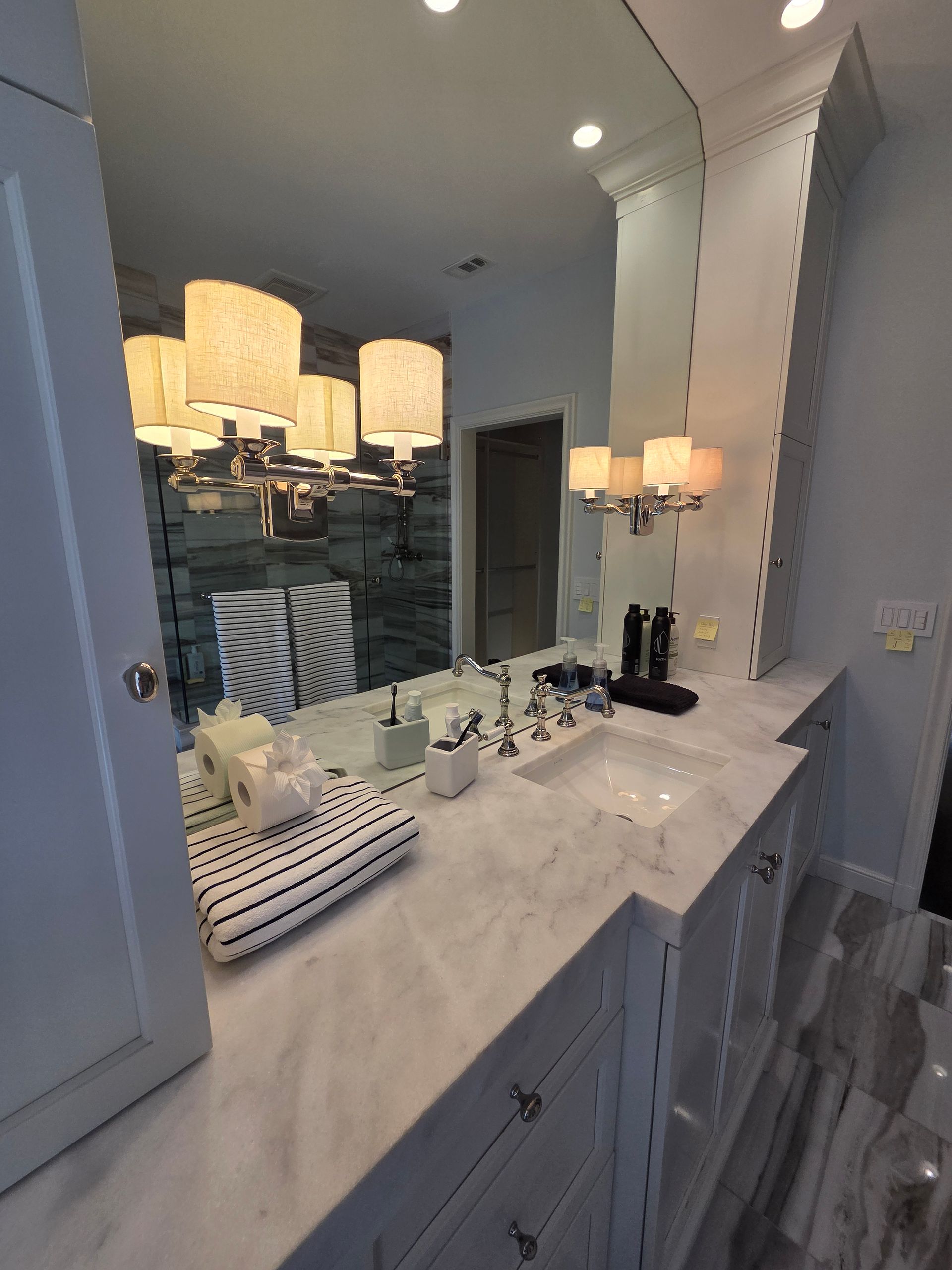Bathroom with marble countertop, large mirror, and multiple light fixtures.