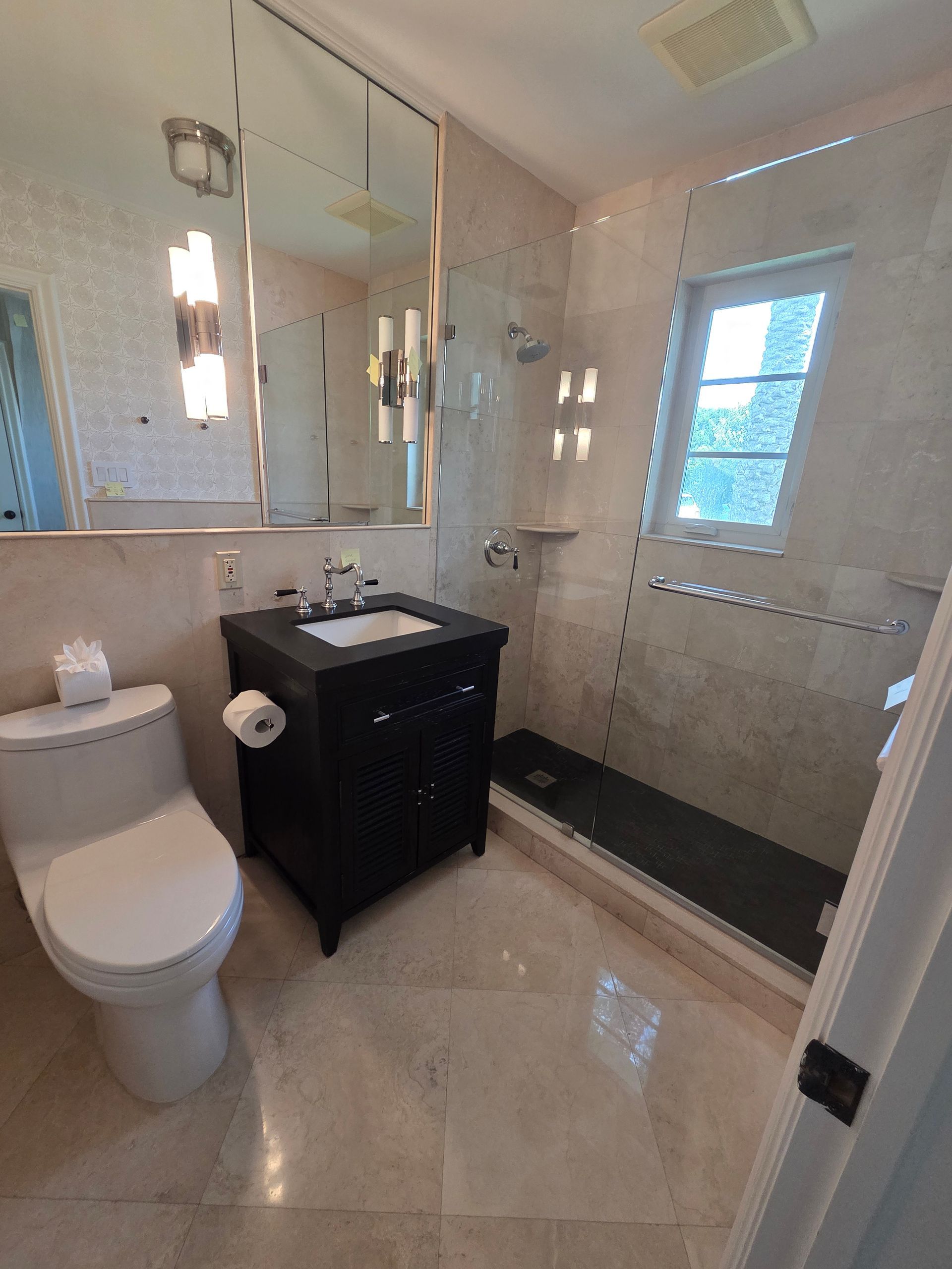 Bathroom with black vanity, toilet, shower, and window. Beige tile walls and floor.