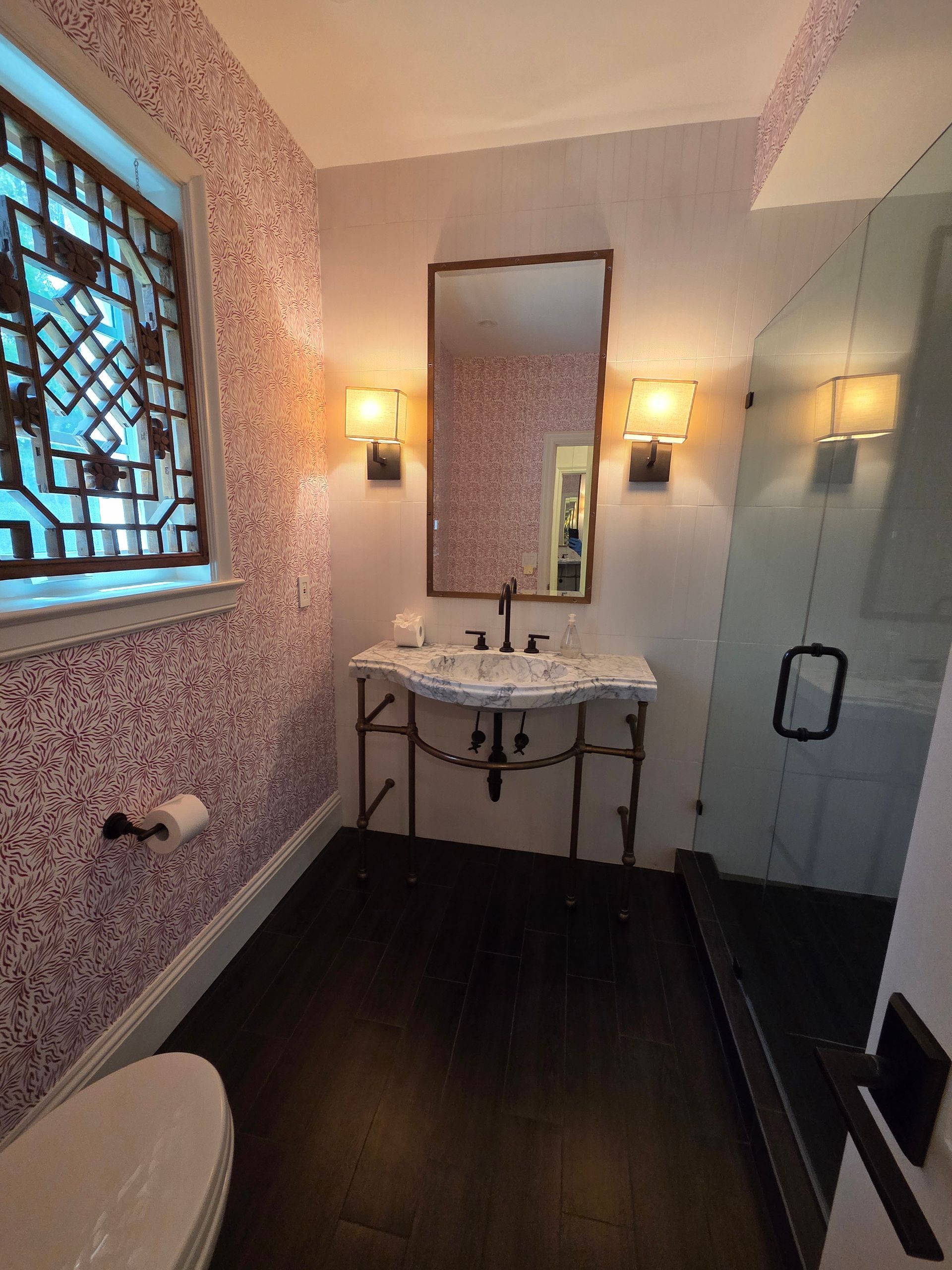 Bathroom with patterned pink walls, dark wood floor, vanity, and decorative window.