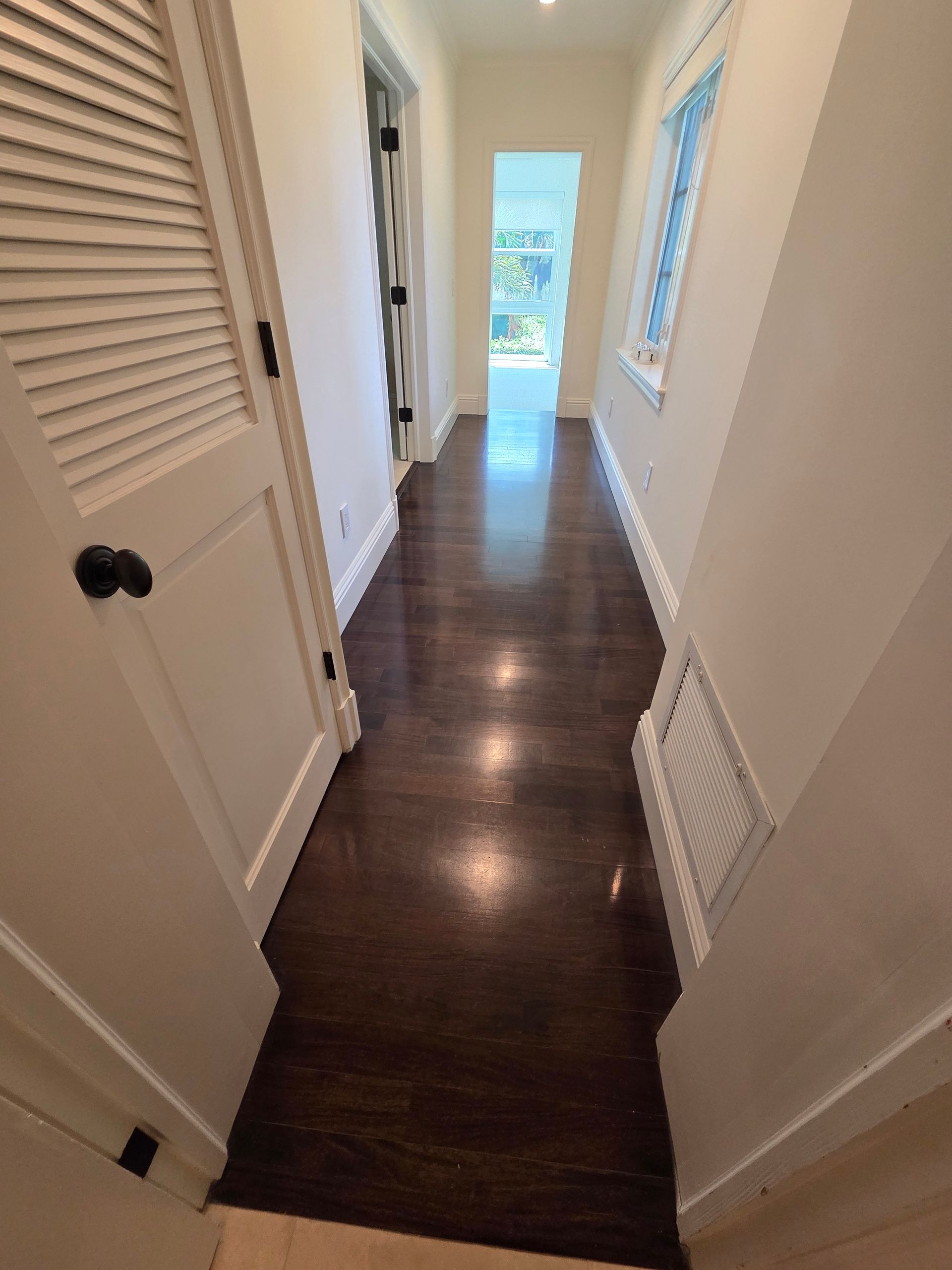Narrow hallway with dark wood floors, white walls, and a door on the left.