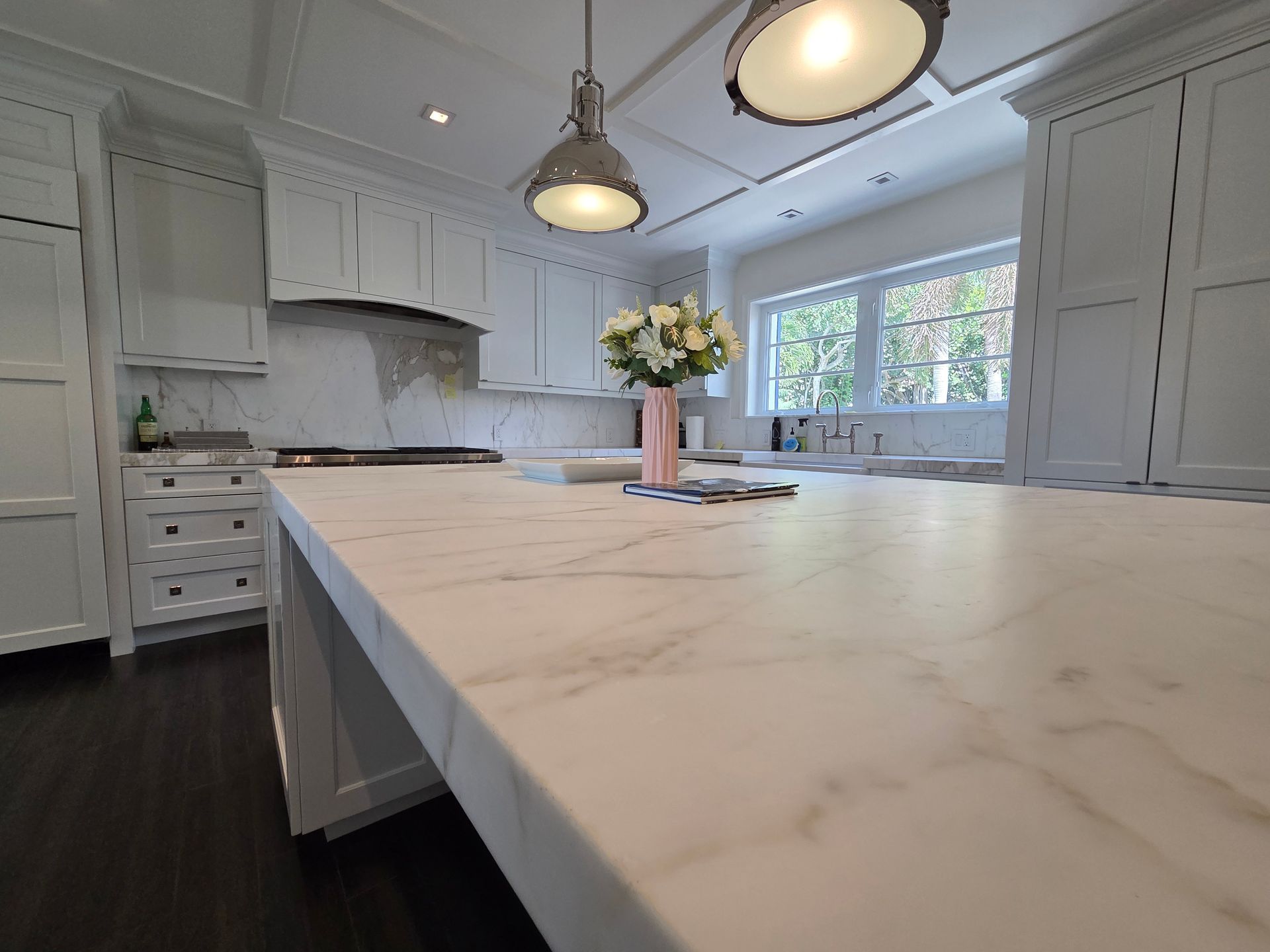 Marble countertop in a bright white kitchen with overhead lighting and a flower vase.