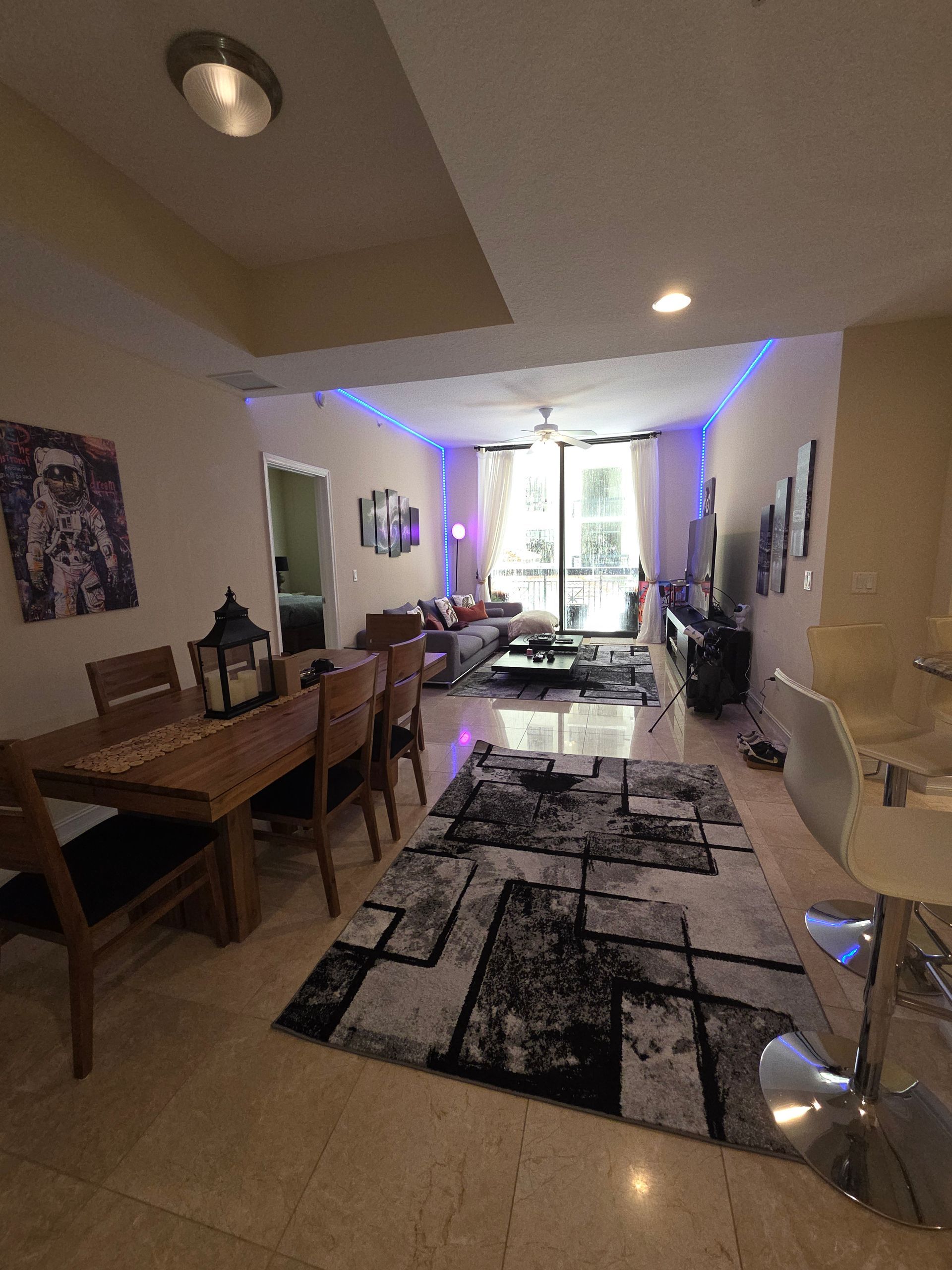 Dining room with wooden table, rug, and view of living area with large windows.