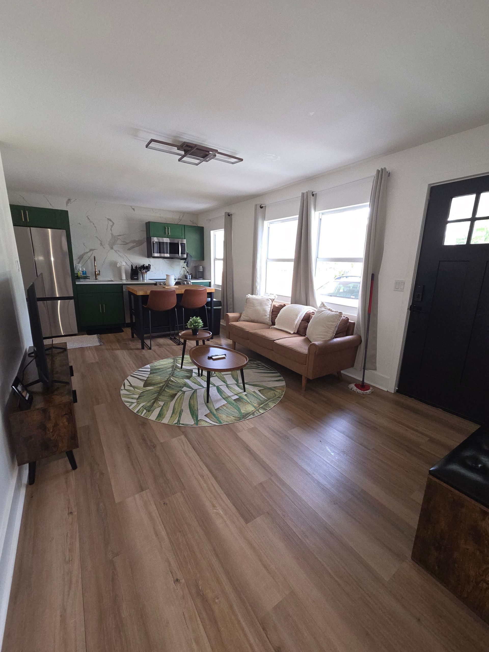 Living room with tan couch, green kitchen, wooden floors, and round rug.