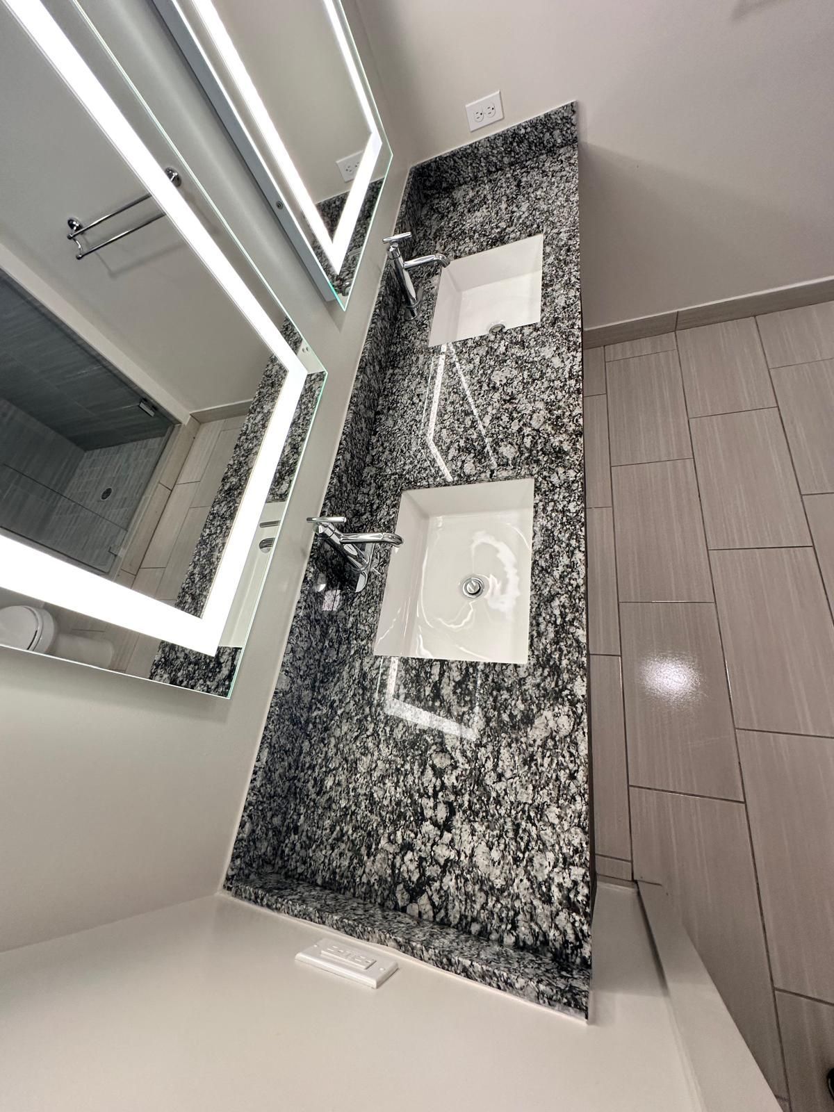 Bathroom with two square sinks set into a black and white patterned countertop, next to a large mirror.