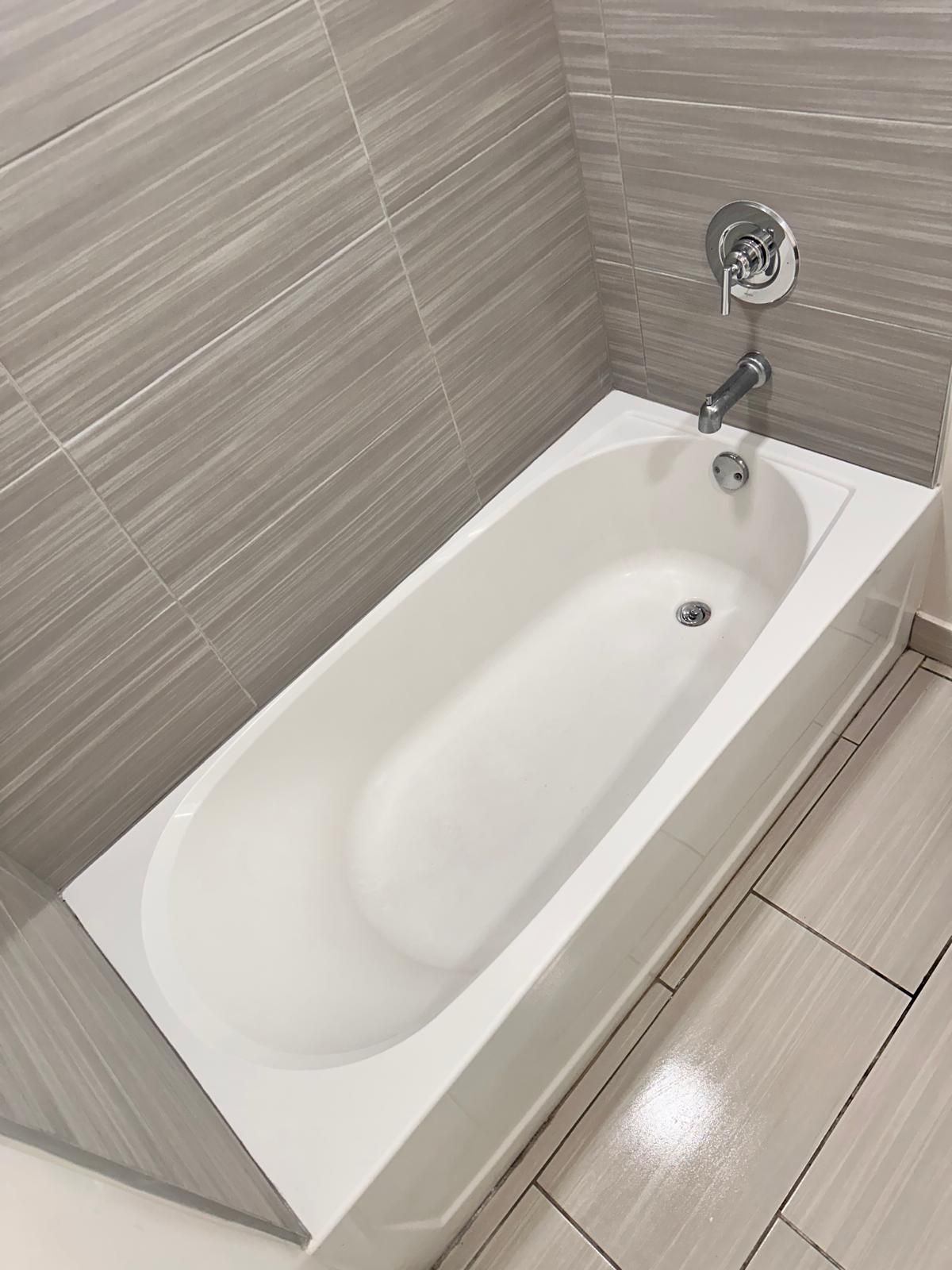 White bathtub in a modern bathroom with gray tiled walls and floor.