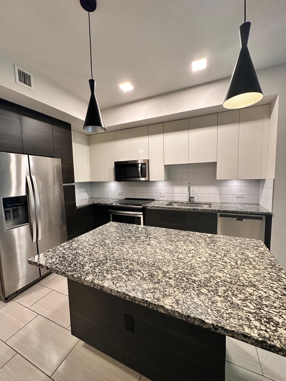 Modern kitchen with stainless steel appliances, dark cabinets, and granite island countertop.