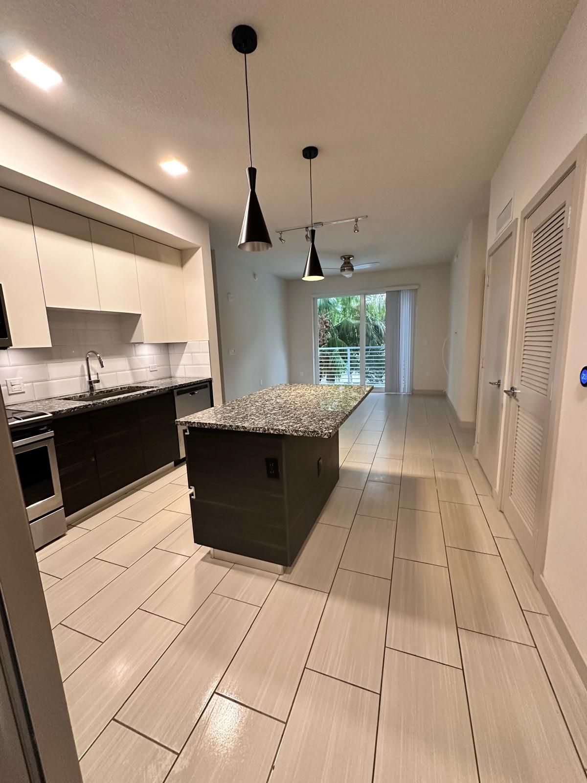 Kitchen with island and pendant lights, leading to a living area and balcony.