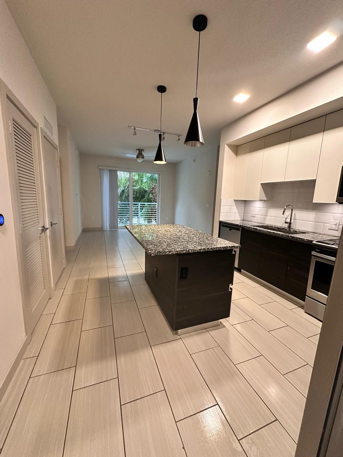Modern kitchen with dark cabinetry, large island with granite countertop, and light tile flooring.